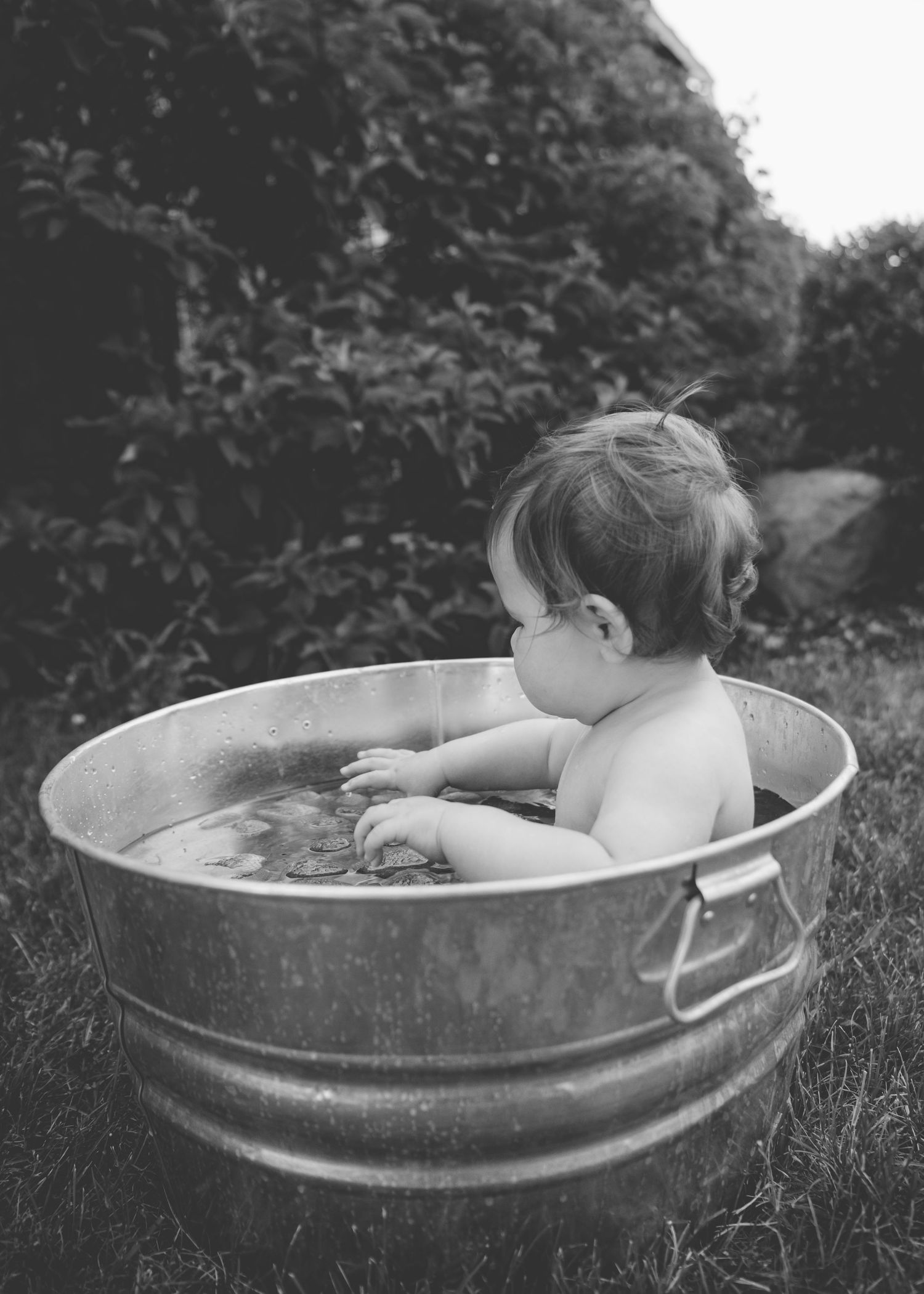 A photo series shows someone dunking their head underwater in a metal tub outdoors on grass.