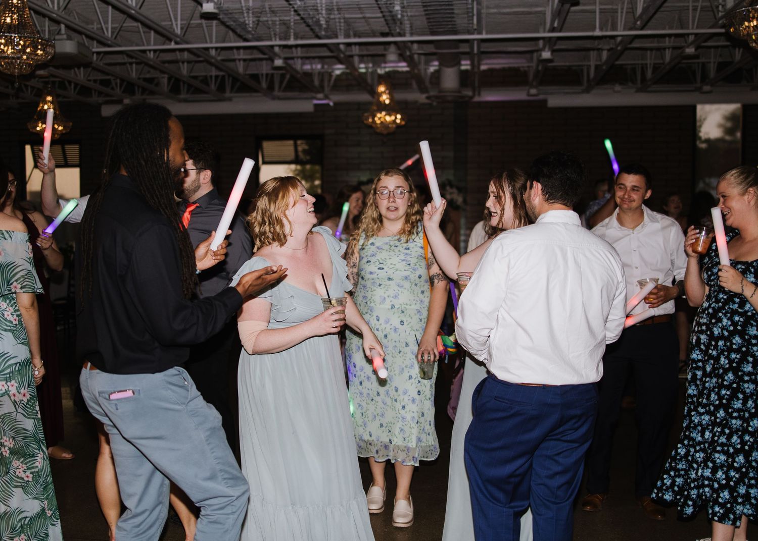 People dance and celebrate at a wedding reception in an indoor venue with ambient lighting.