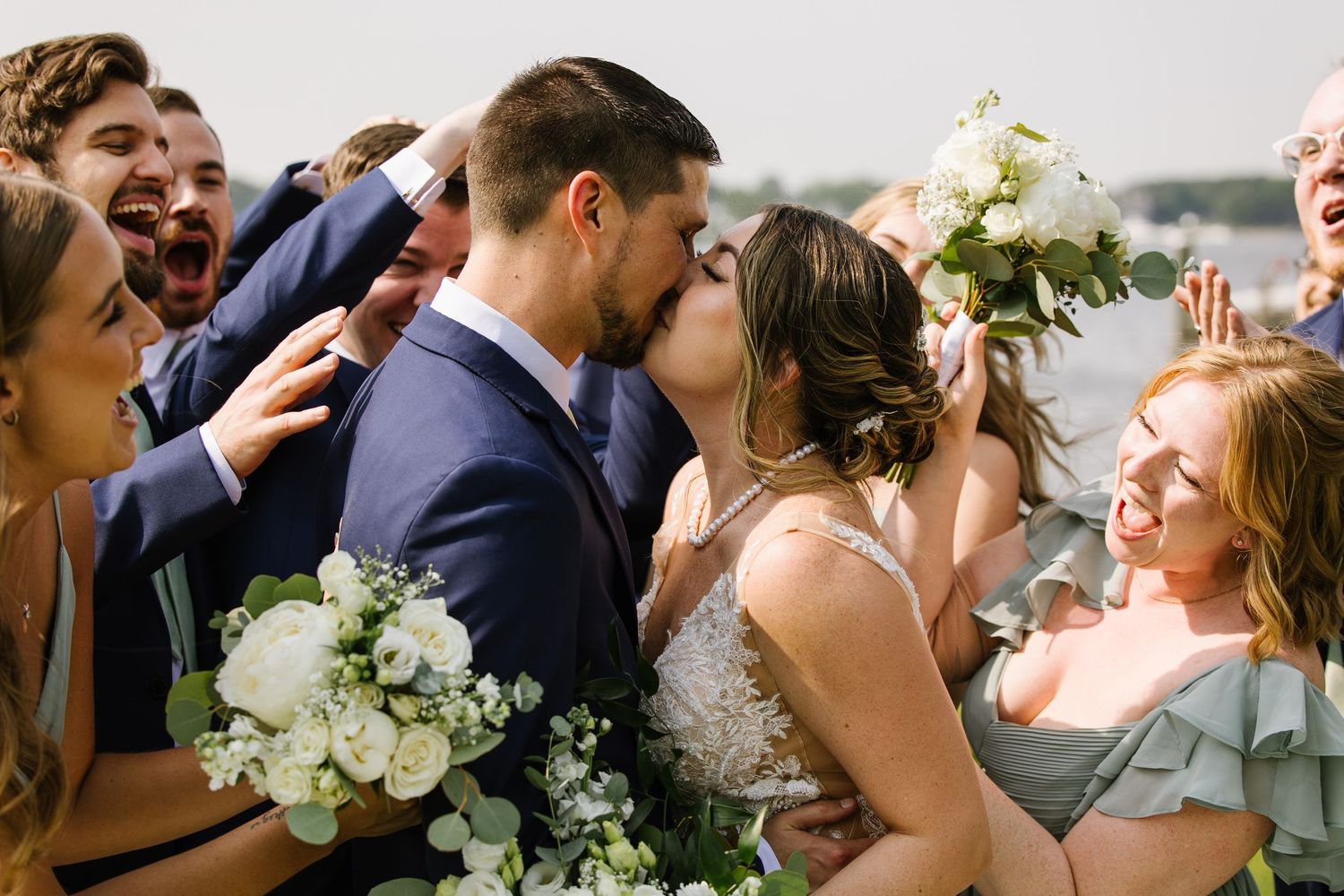 A joyous wedding celebration features the newlyweds sharing a kiss while guests cheer with white floral bouquets in view.