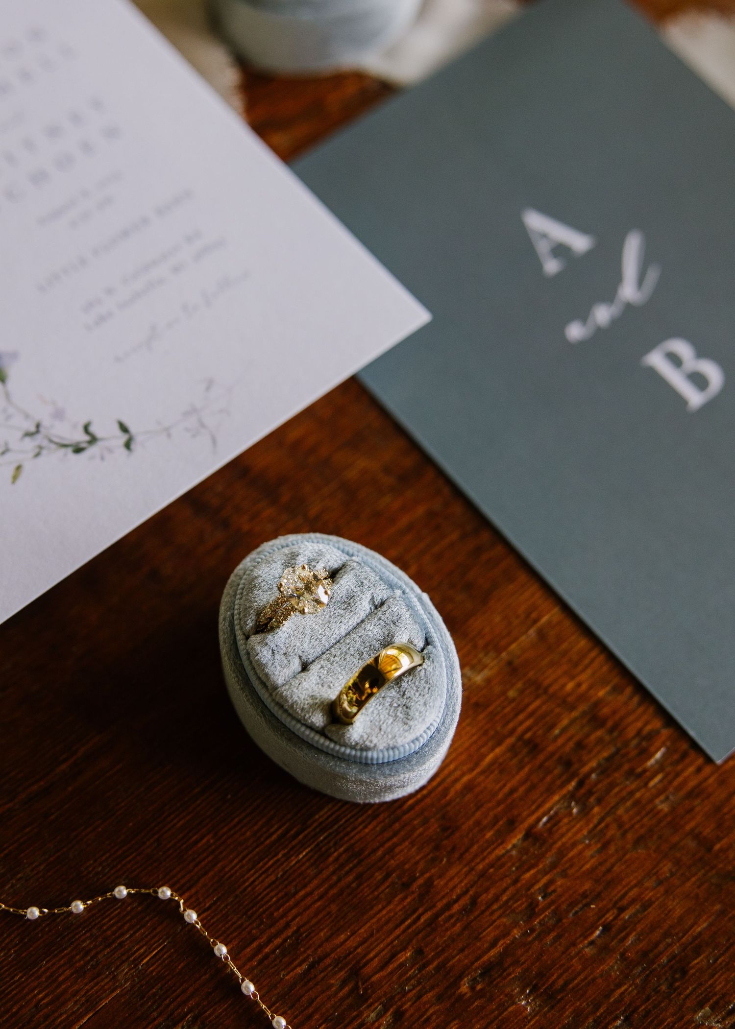 A vintage silver ring box with delicate jewelry pieces displayed on a dark wooden surface next to paper cards.