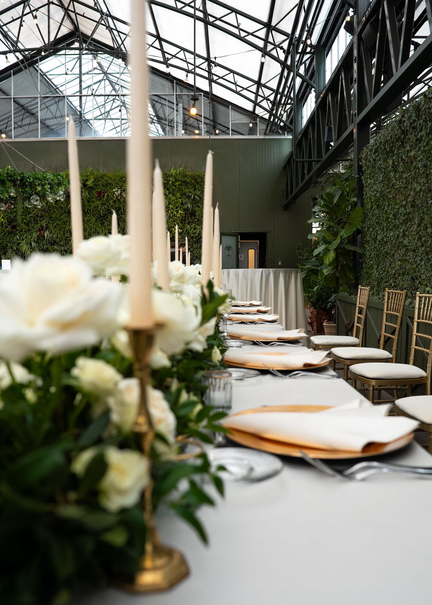 Elegant wedding reception table with white roses, gold candelabras, and chiavari chairs in a greenhouse venue.