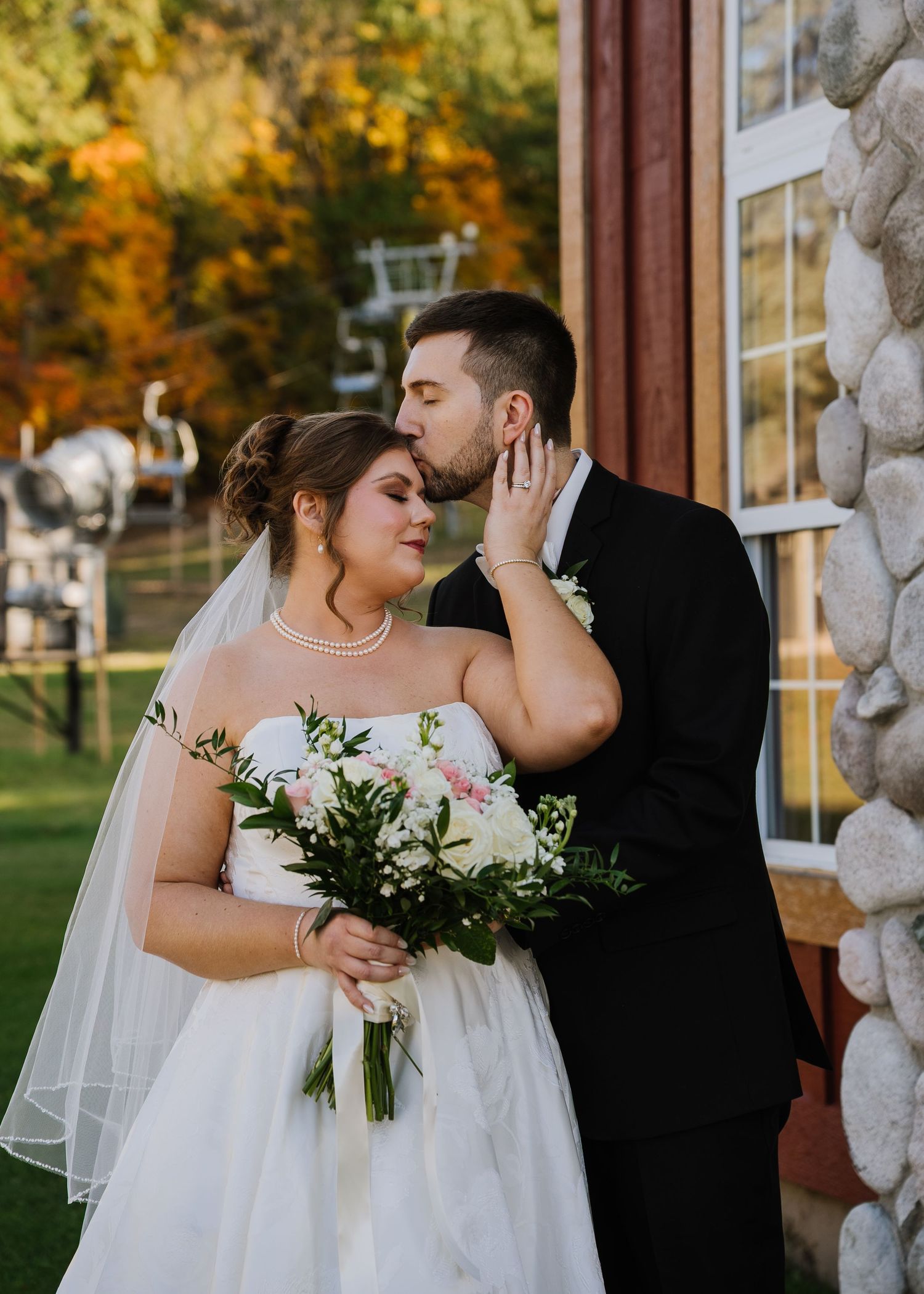 A romantic moment between newlyweds holding a white bouquet during an autumn outdoor wedding ceremony.