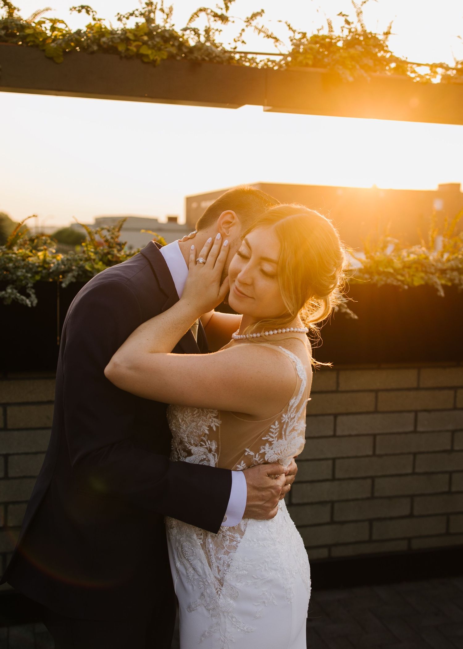 Romantic couple dancing together outdoors against a golden sunset with brick wall background.