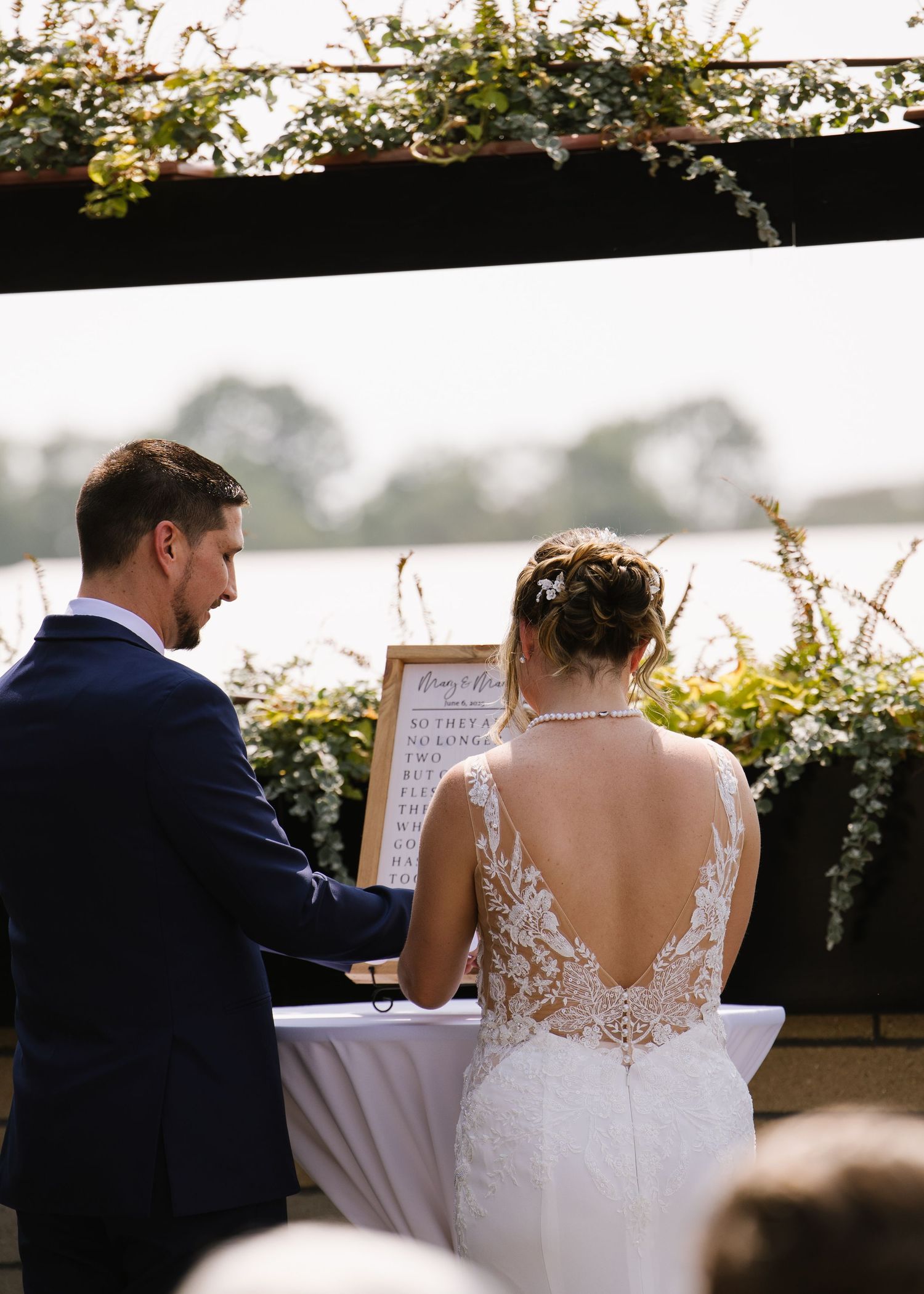 Couple signing marriage documents at an outdoor wedding ceremony with lace back dress and navy suit.