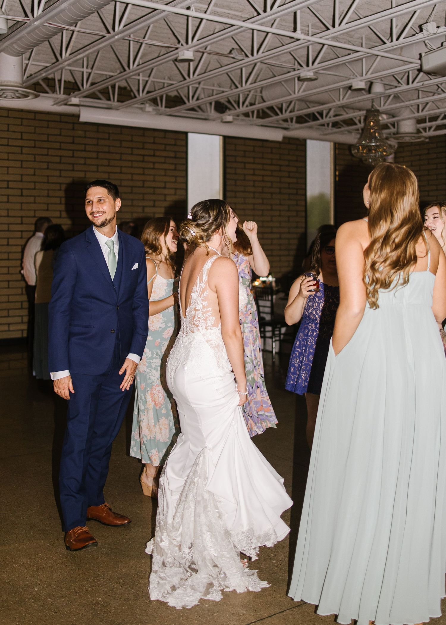 Wedding party members dancing and celebrating in reception venue with industrial ceiling and brick walls.