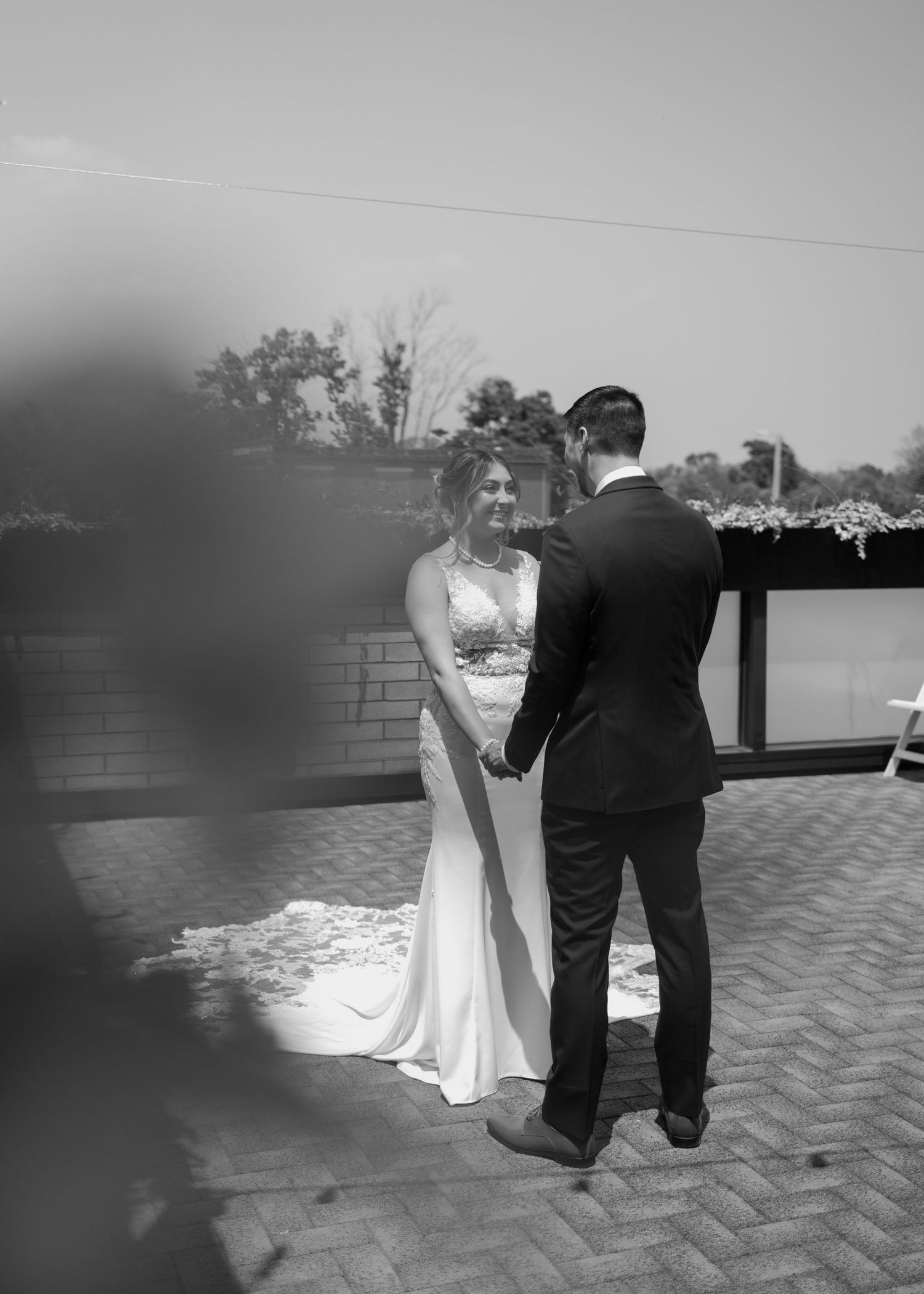 A black and white wedding photo shows a couple dancing together on an outdoor patio surrounded by brick walls.