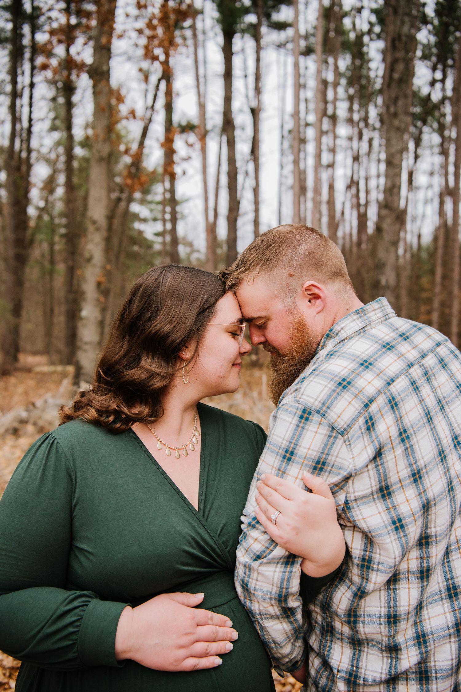 A couple shares an intimate forehead touch while posing in a winter forest setting.