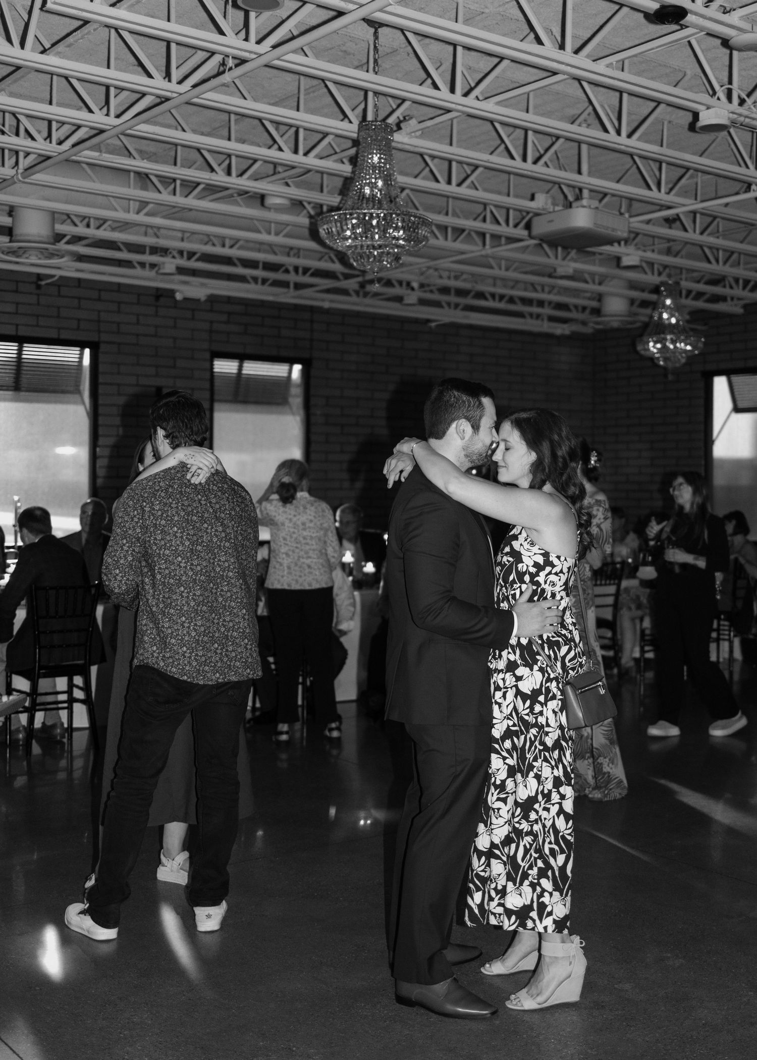 Couples dance together at an indoor venue with exposed brick walls, chandeliers, and an industrial ceiling.