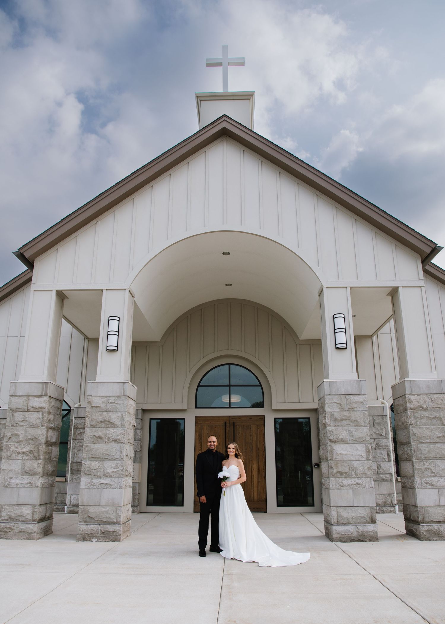 A white wedding chapel with stone columns and a cross on top features an arched entrance and elegant architecture.