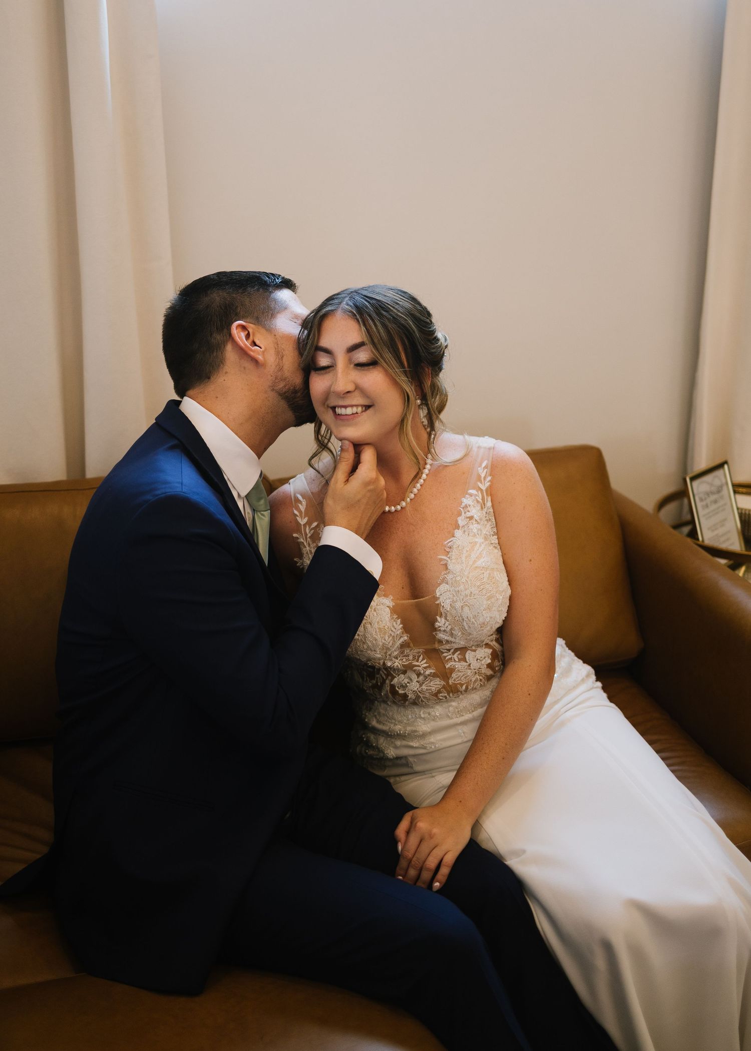 A couple shares an intimate moment on a brown leather couch in a minimalist indoor setting.