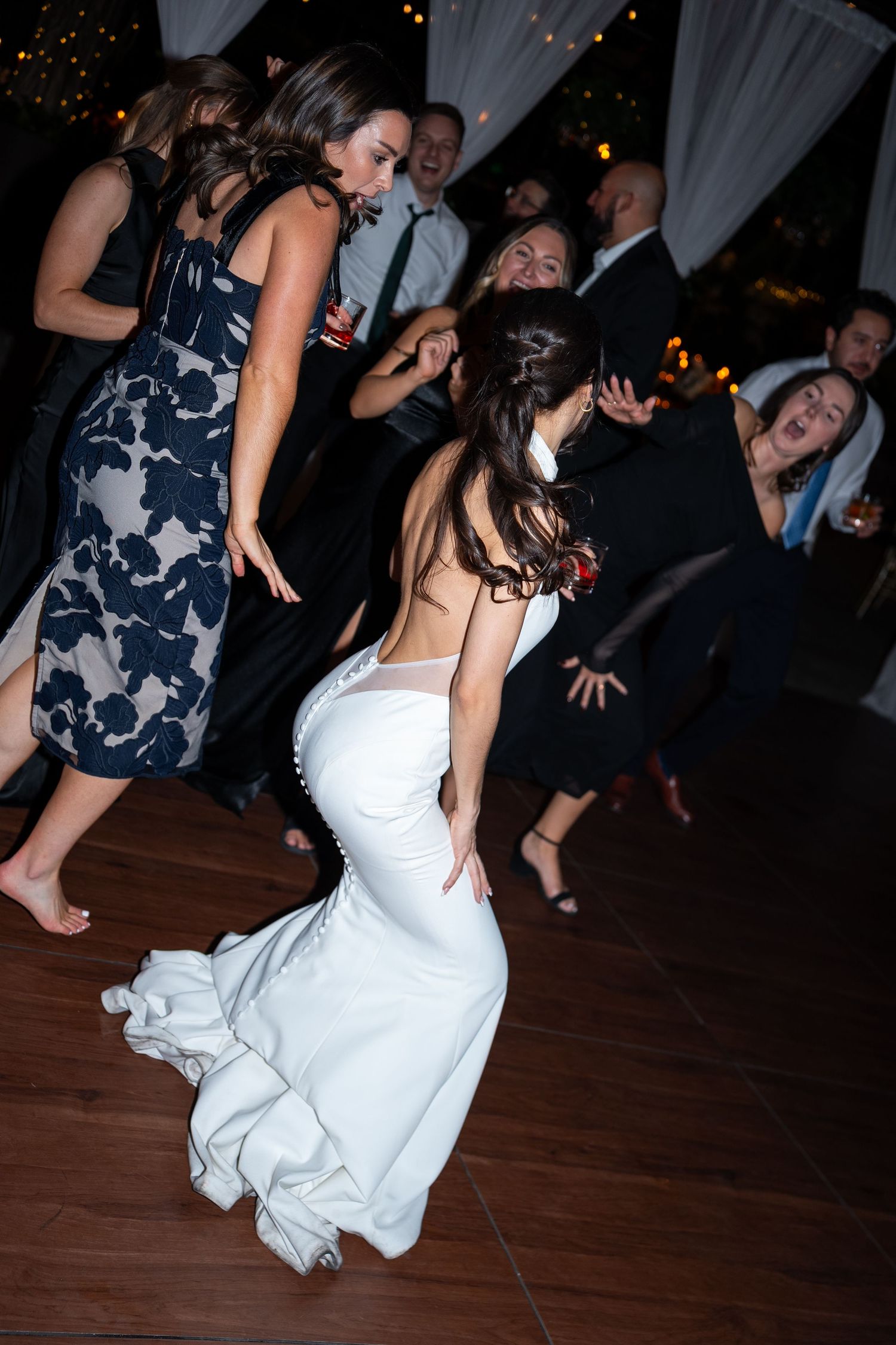 Bride in white mermaid gown dancing energetically at wedding reception with guests celebrating on dance floor.