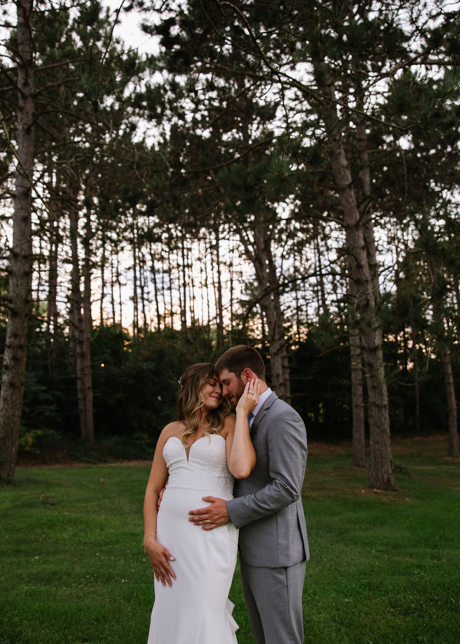 Couple sharing an intimate moment in the woods at sunset against a backdrop of tall pine trees.