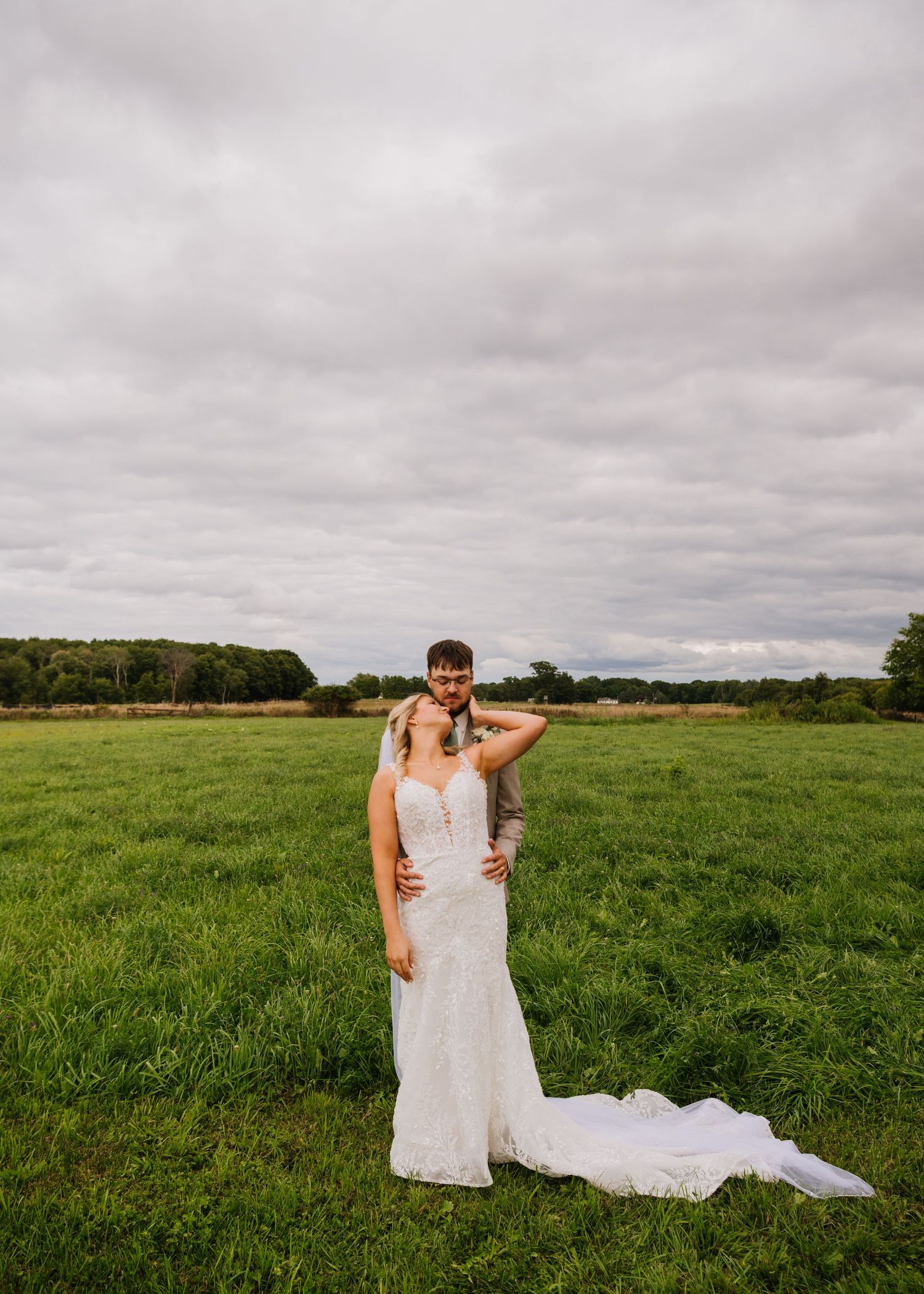 A panoramic view of a person in a flowing white wedding dress standing in a lush green meadow under cloudy skies.