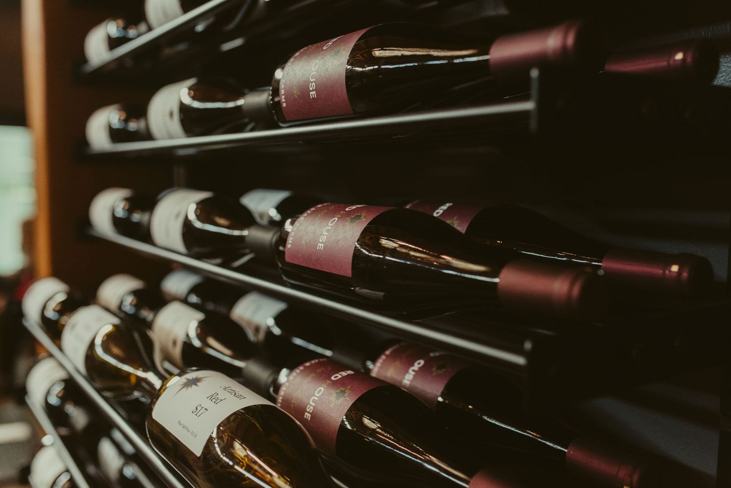 Wine bottles arranged in rows on dark wooden storage racks in a dimly lit cellar or wine room.