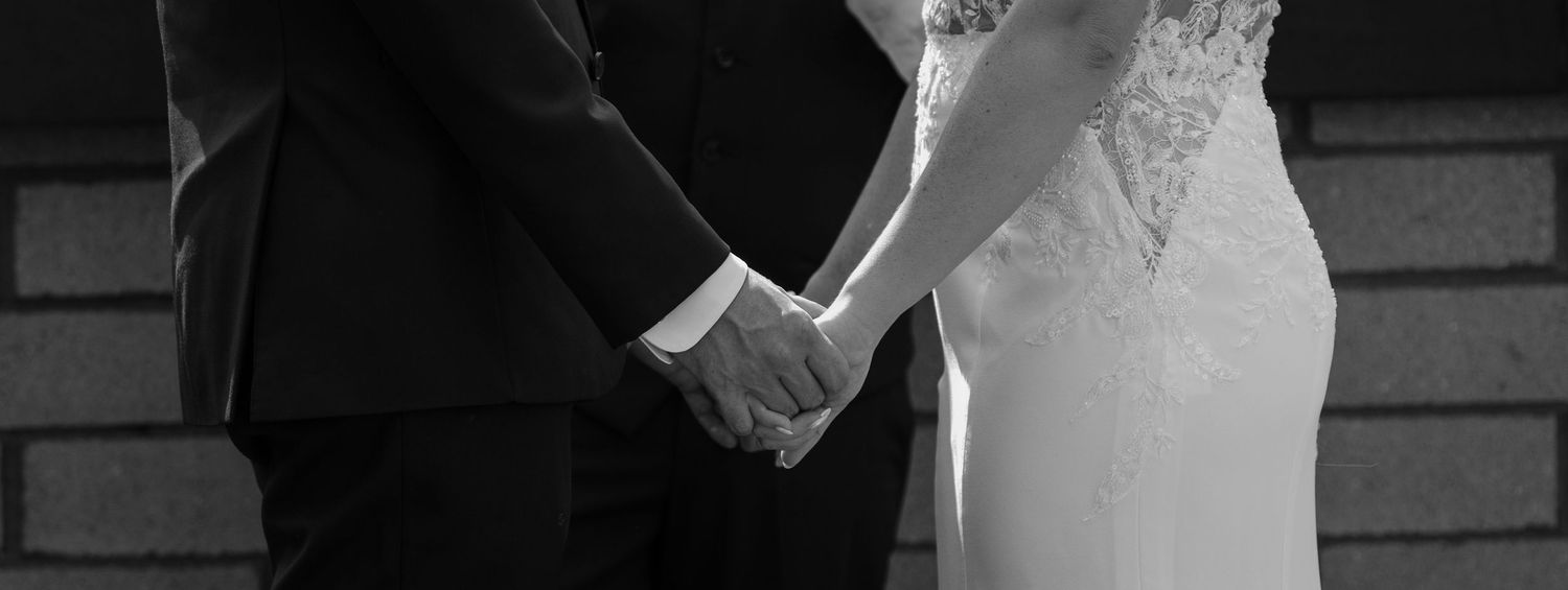 Black and white image showing a couple in wedding attire holding hands together.