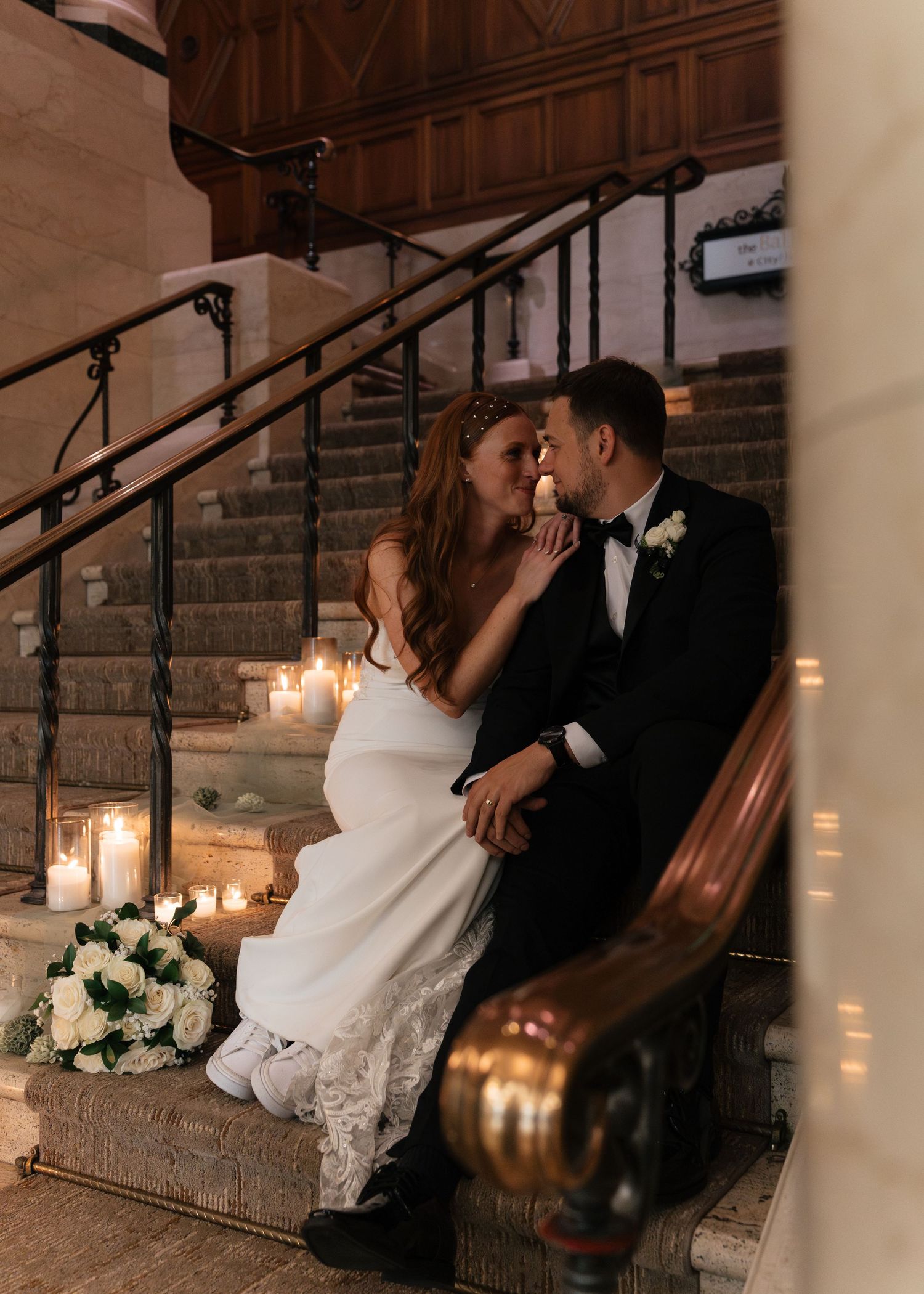 Bride and groom share a romantic moment on candlelit stone stairs, surrounded by white roses at their elegant wedding.