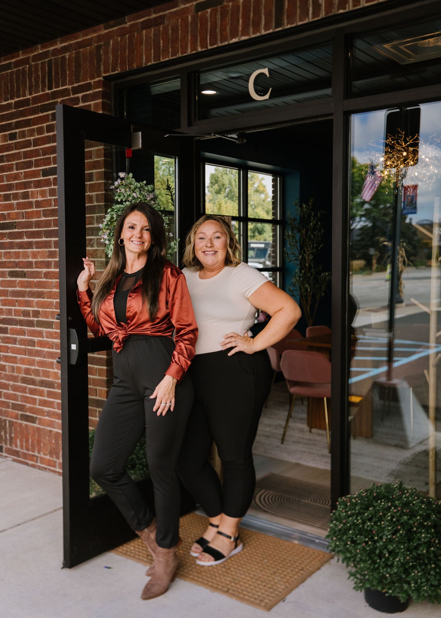 People posing together in front of a brick building entrance with a welcome mat and potted plants.