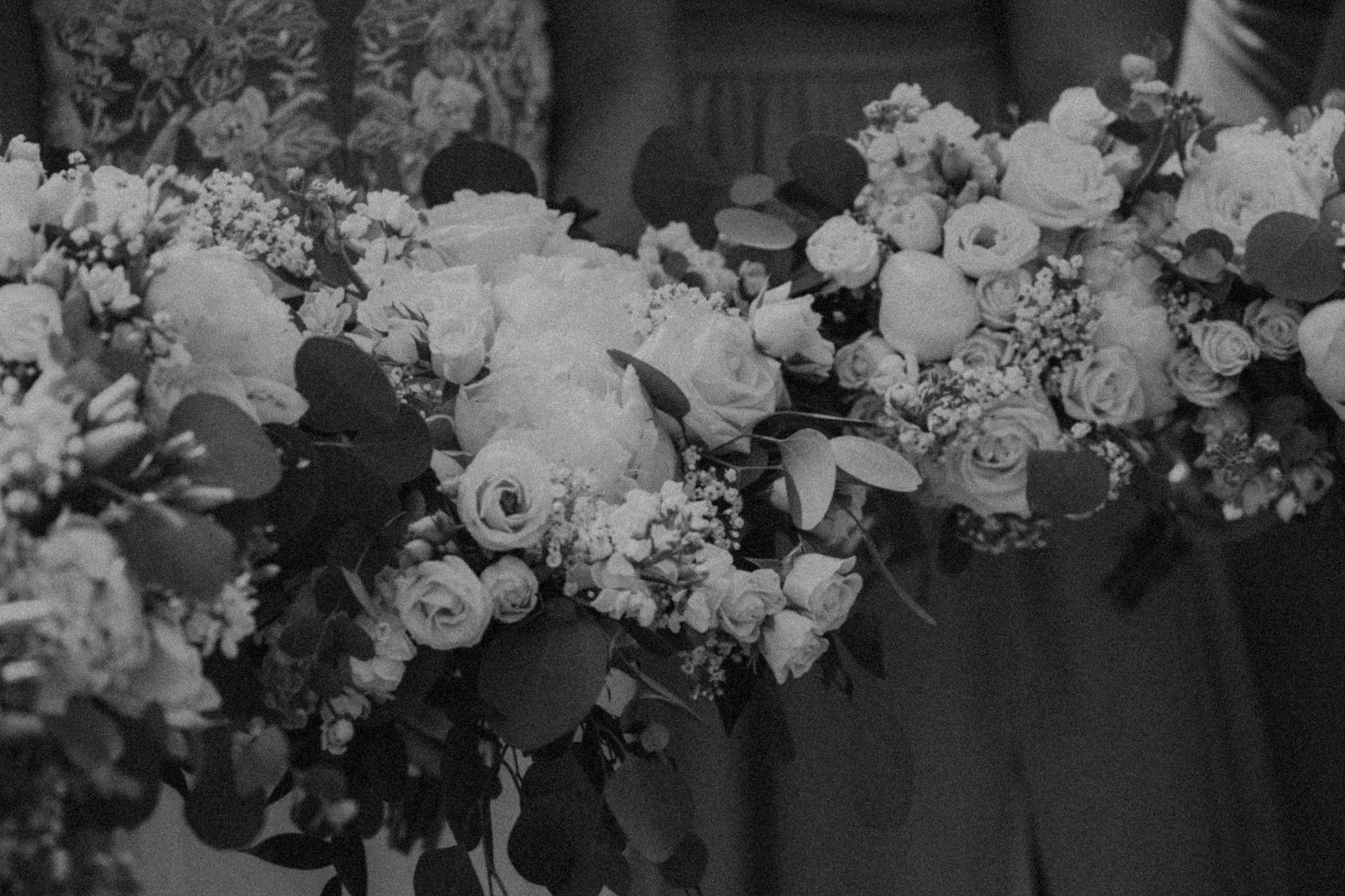 Black and white close-up of lush floral arrangement featuring roses and various white blossoms.
