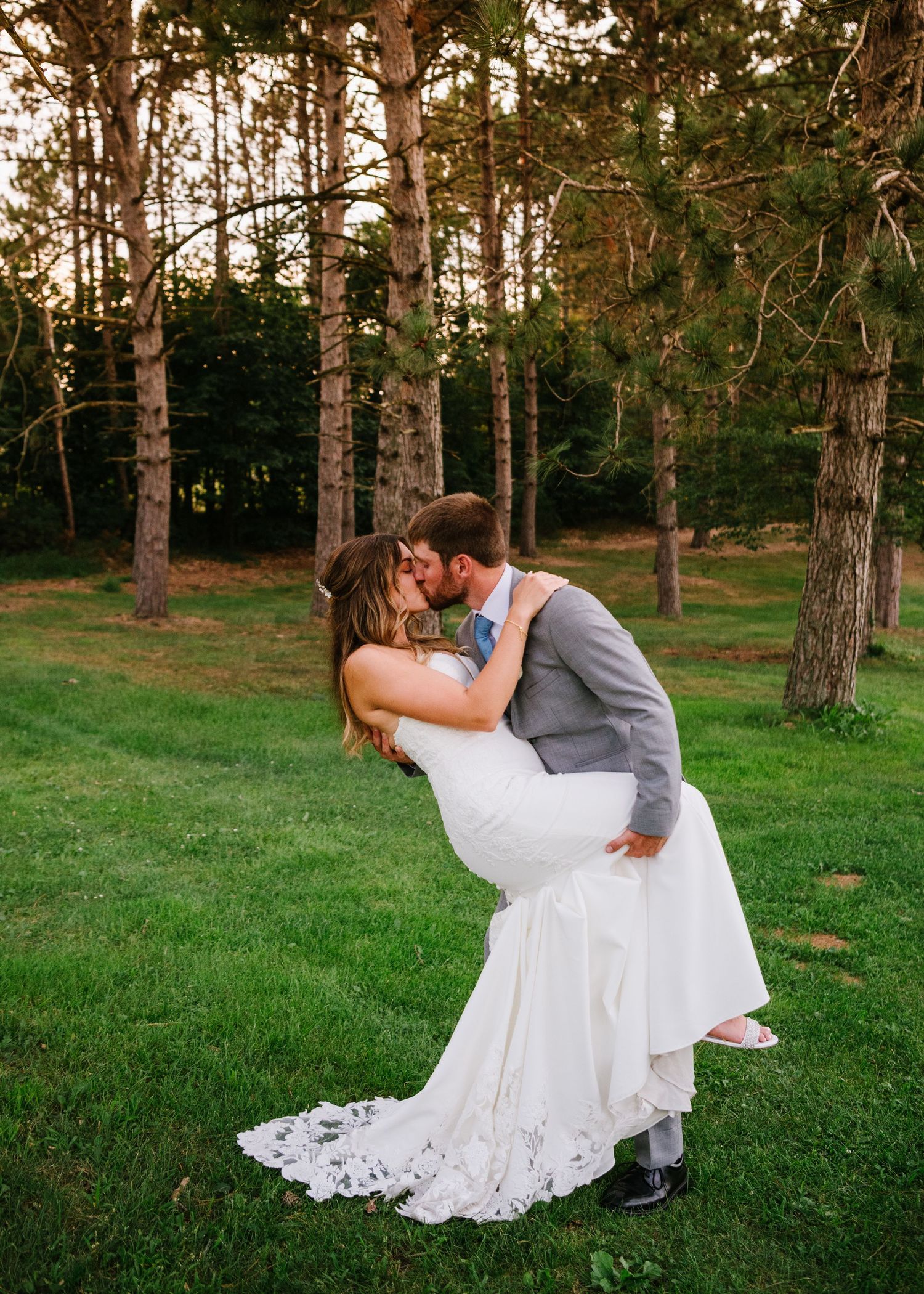 A romantic dip kiss sequence showing couples embracing in a sunset-lit wooded area with tall pine trees and green grass.