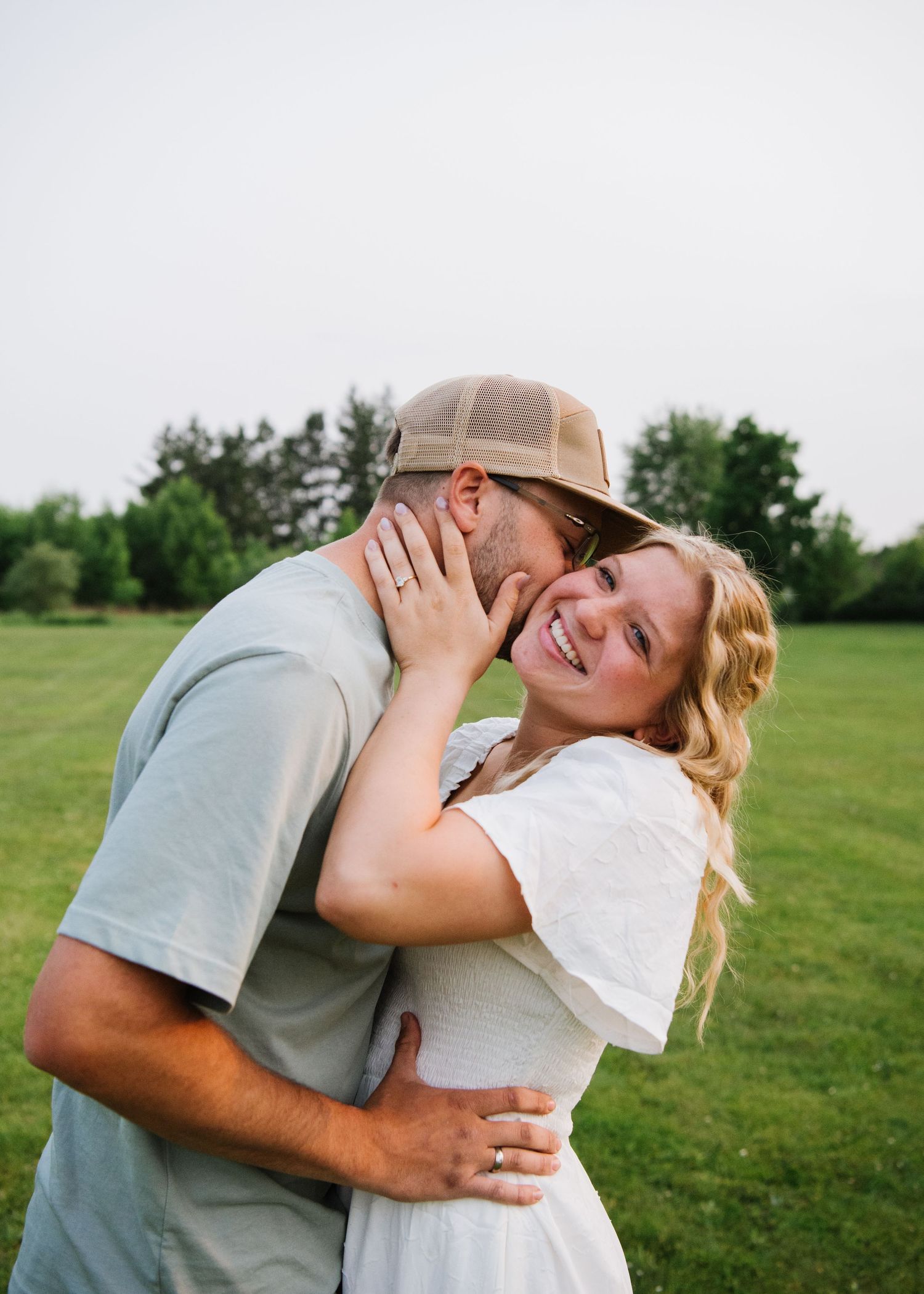 A playful romantic moment captured between a couple embracing in a grassy field on a summer day.