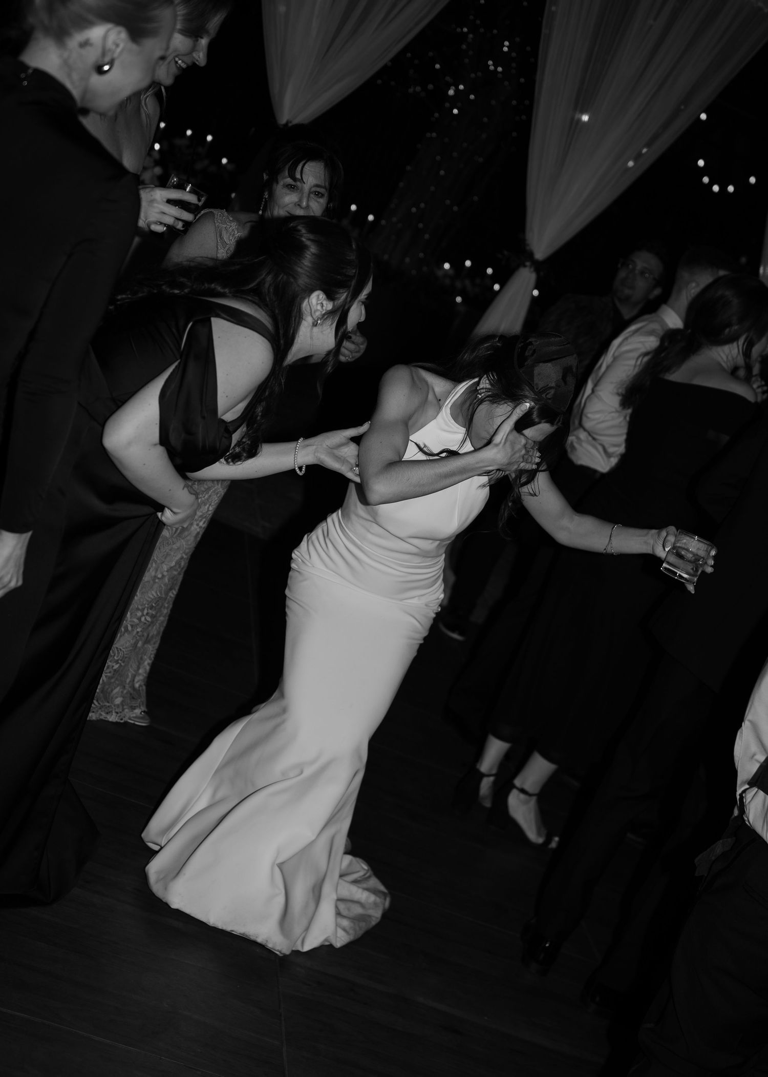 Black and white photo of a bride in white gown dancing and dipping at a wedding reception celebration.
