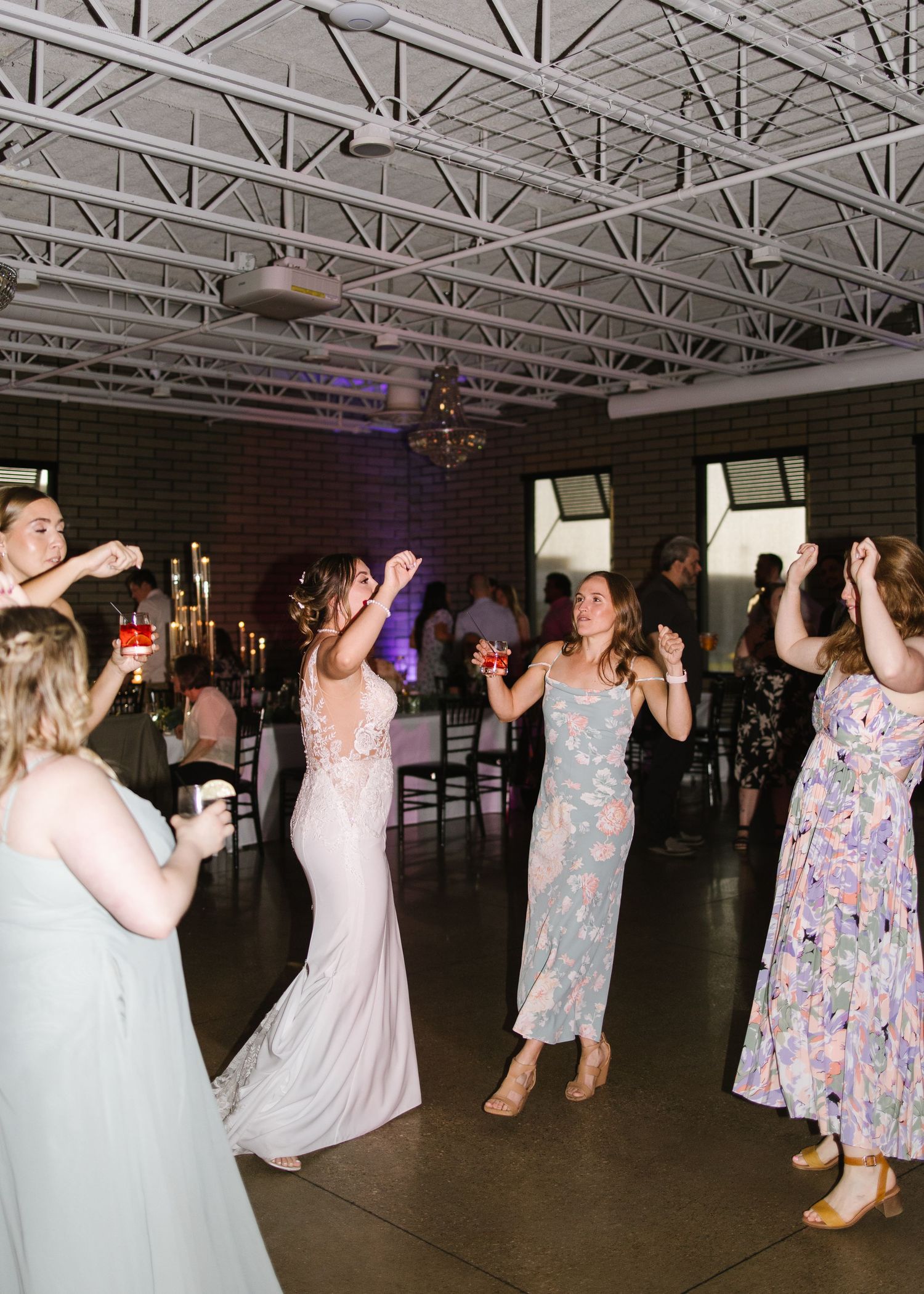 A panoramic view of party guests dancing in a large venue with exposed ceiling beams and industrial lighting.