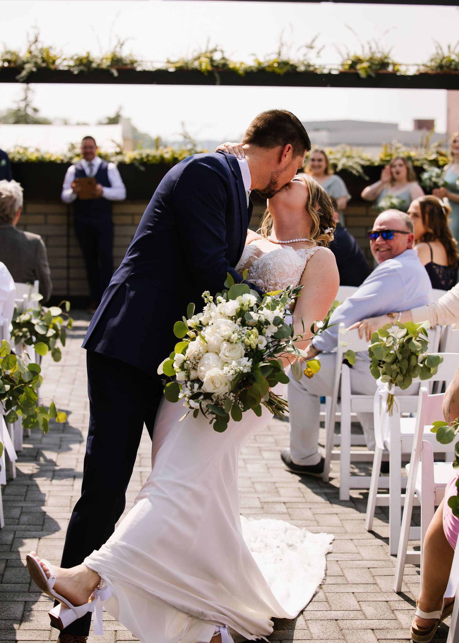 Couple sharing a romantic moment during outdoor wedding ceremony with floral decorations and white chairs on patio.