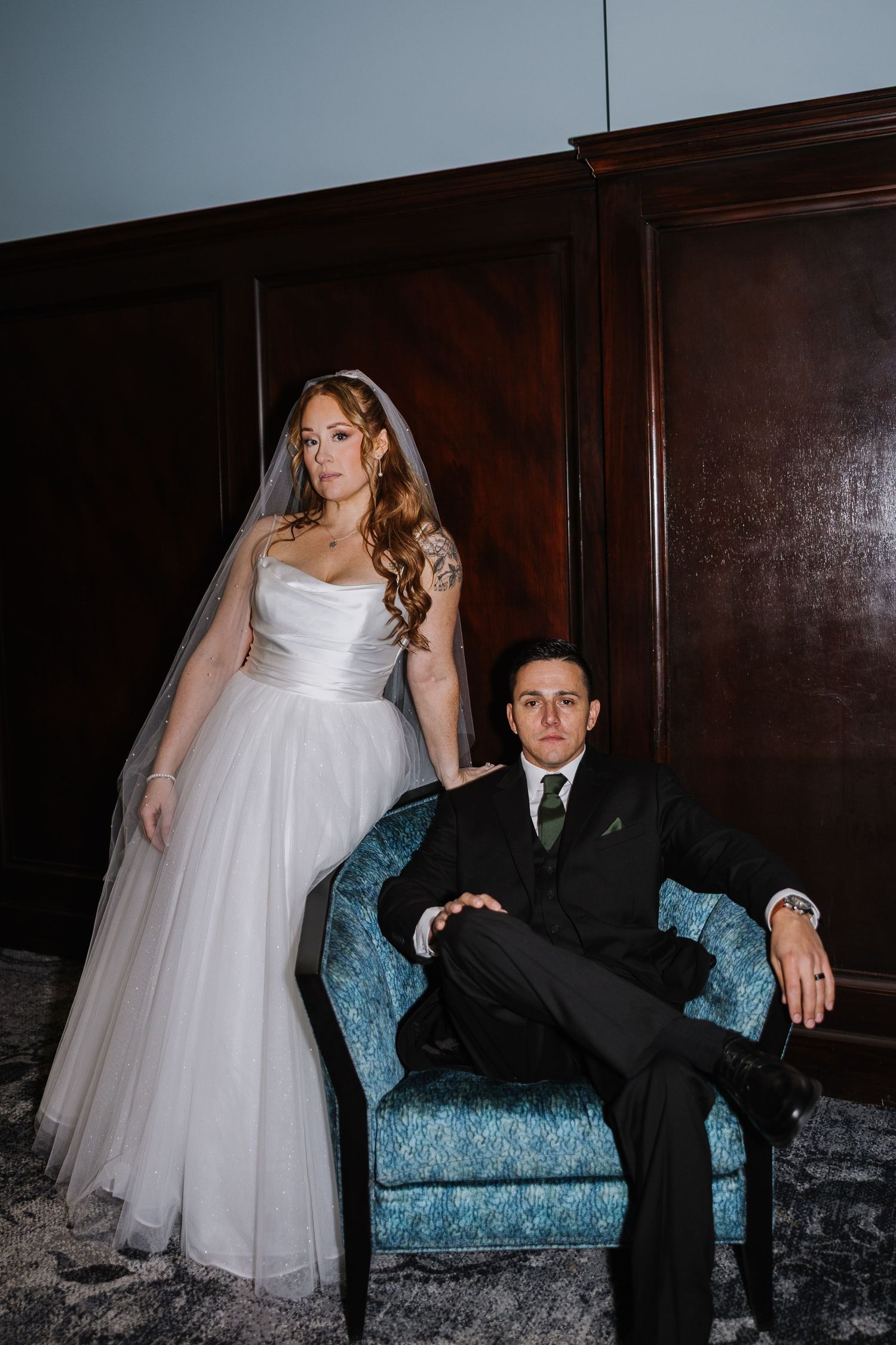Newlywed couple poses on vintage blue damask couch in romantic wedding photography series.