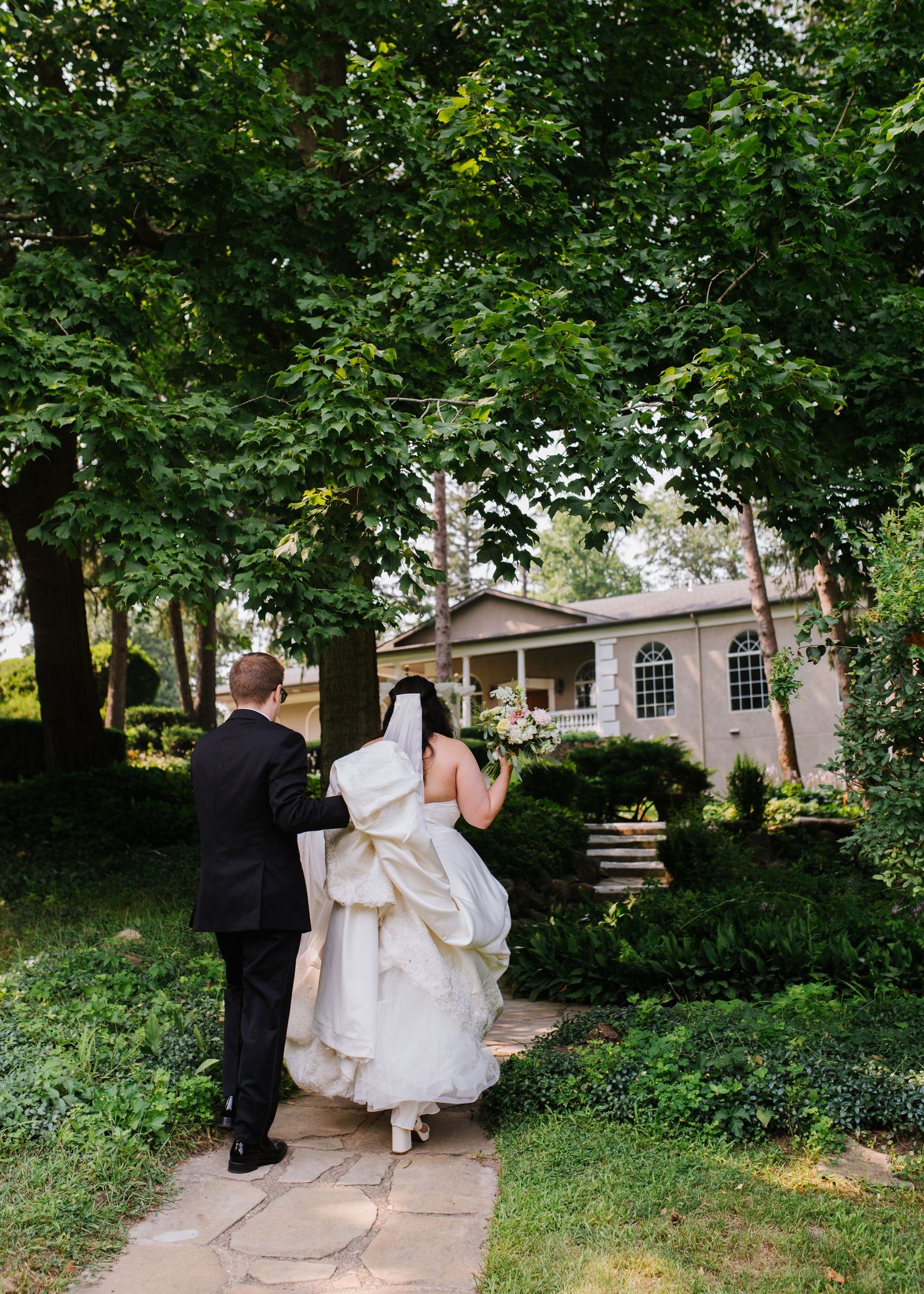 Couple walking along a garden path through lush greenery in formal wedding attire.