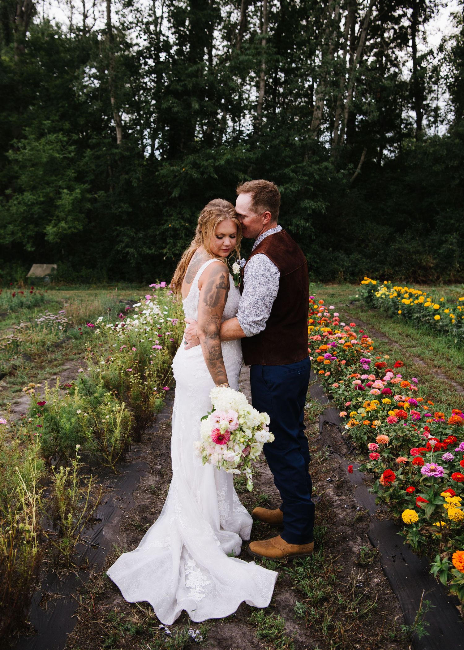 A couple in wedding attire embraces in a garden filled with vibrant orange and yellow flowers.