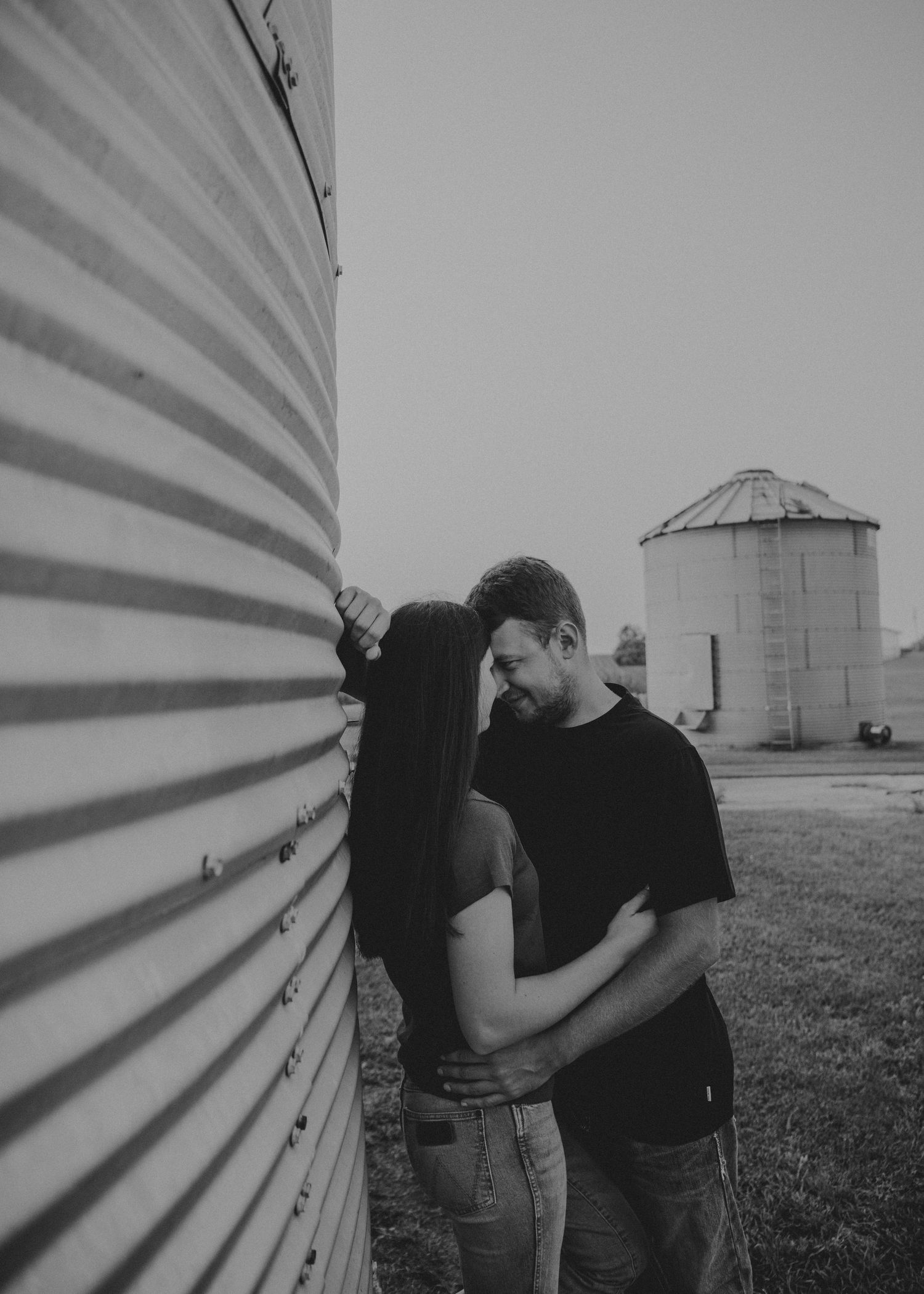 A romantic couple embraces against a white grain silo in a series of black and white photos in rural scenery.