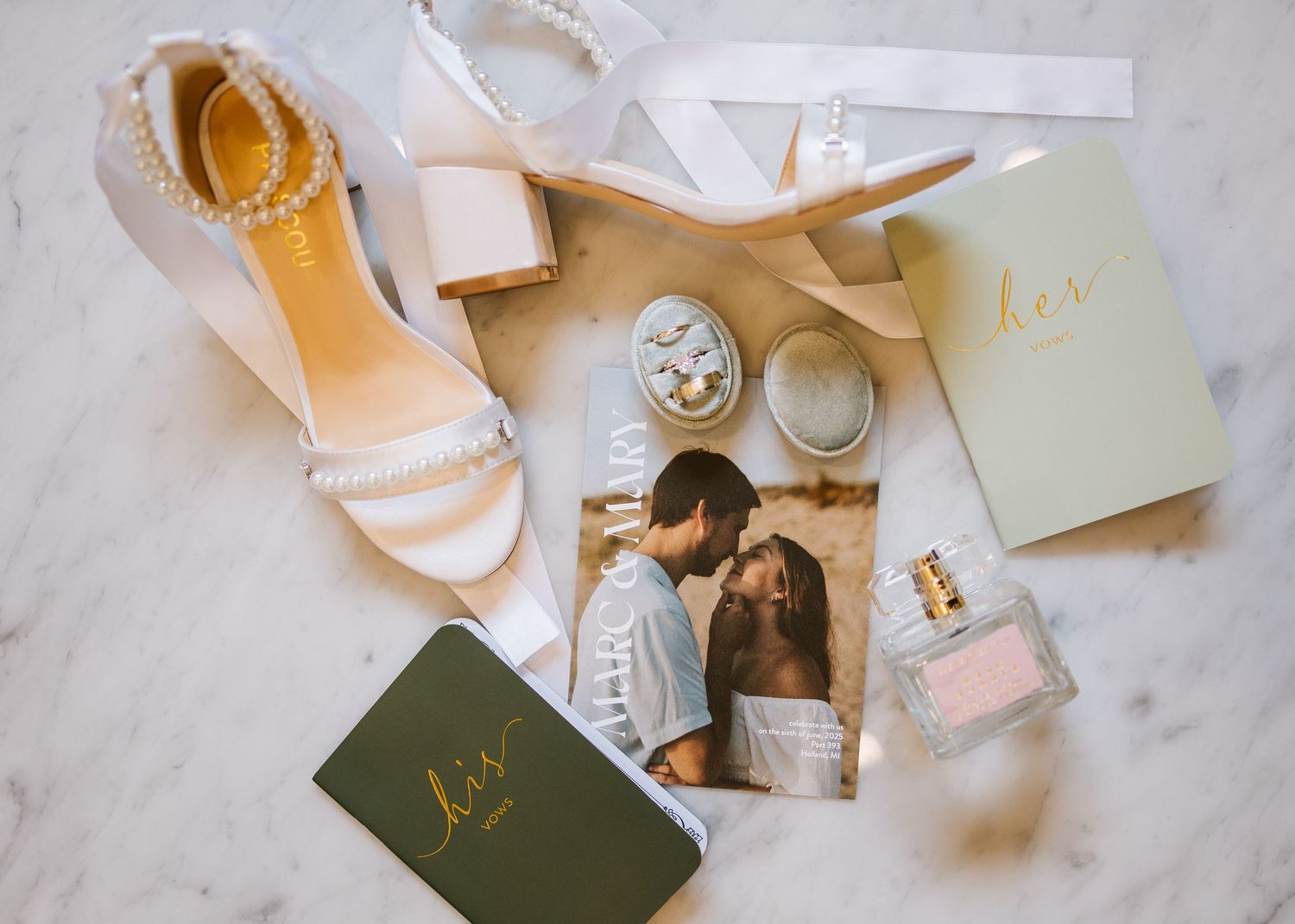 Wedding vignette of elegant invitation cards, floral elements, and silk ribbons on a marble surface.