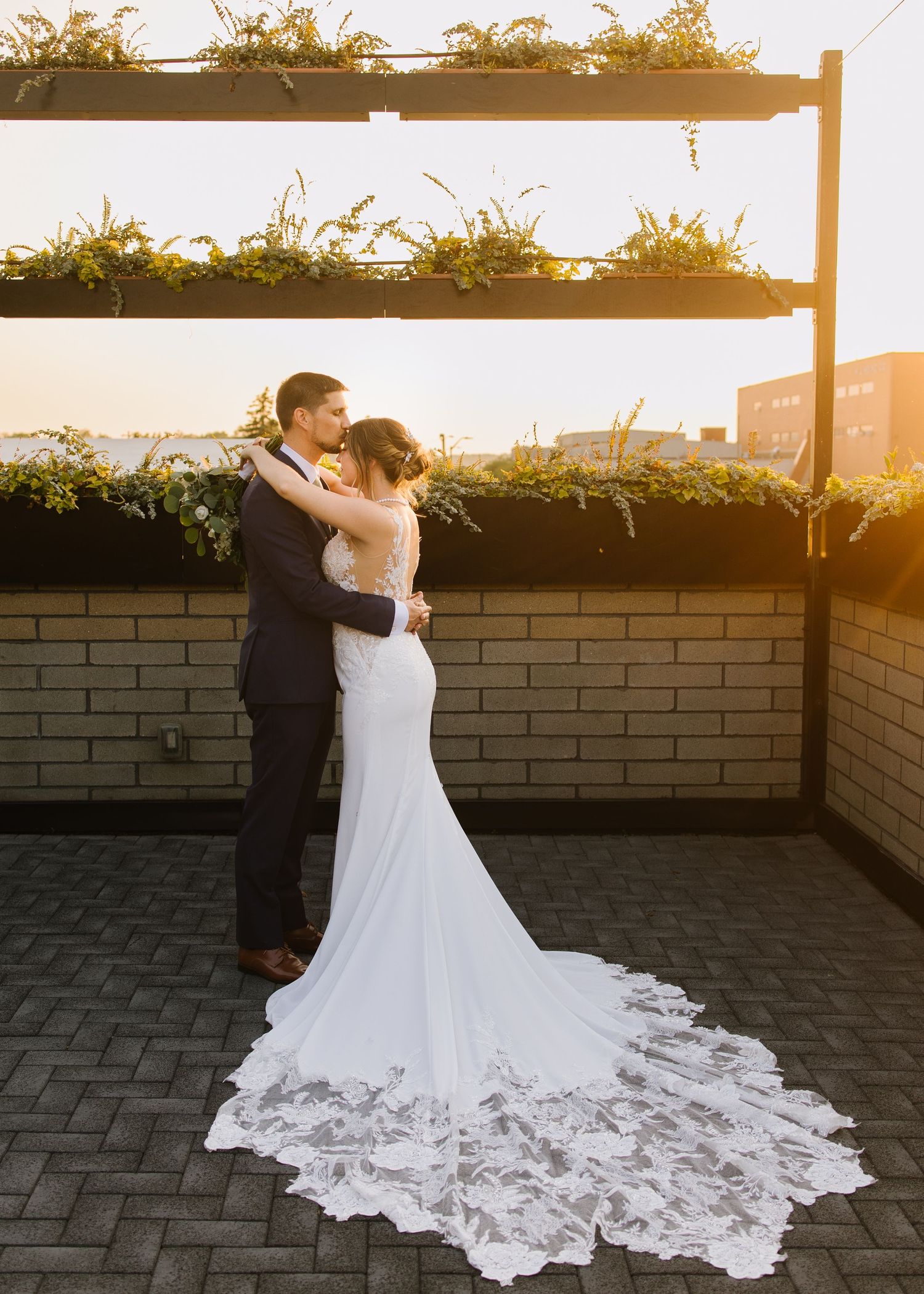 A bride and groom share a tender first dance moment at sunset on a rooftop terrace with brick walls.
