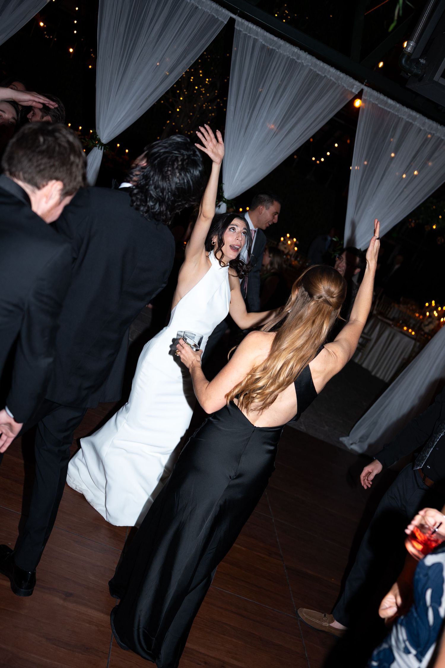 Bride in white gown dancing with guests in black formal wear at elegant wedding reception with draped decor.