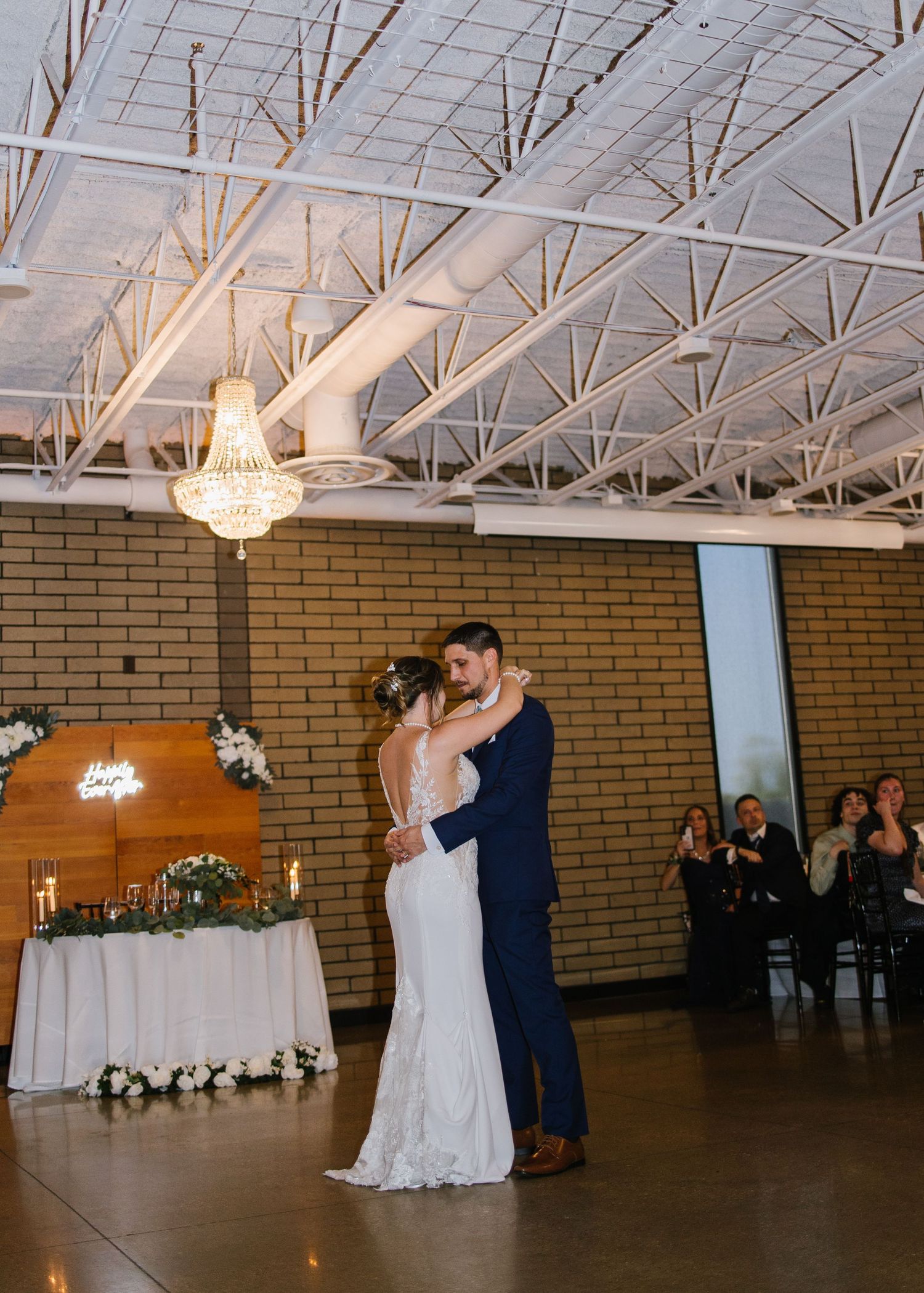Couple sharing their first dance in an elegant reception hall with exposed ceiling and brick walls.