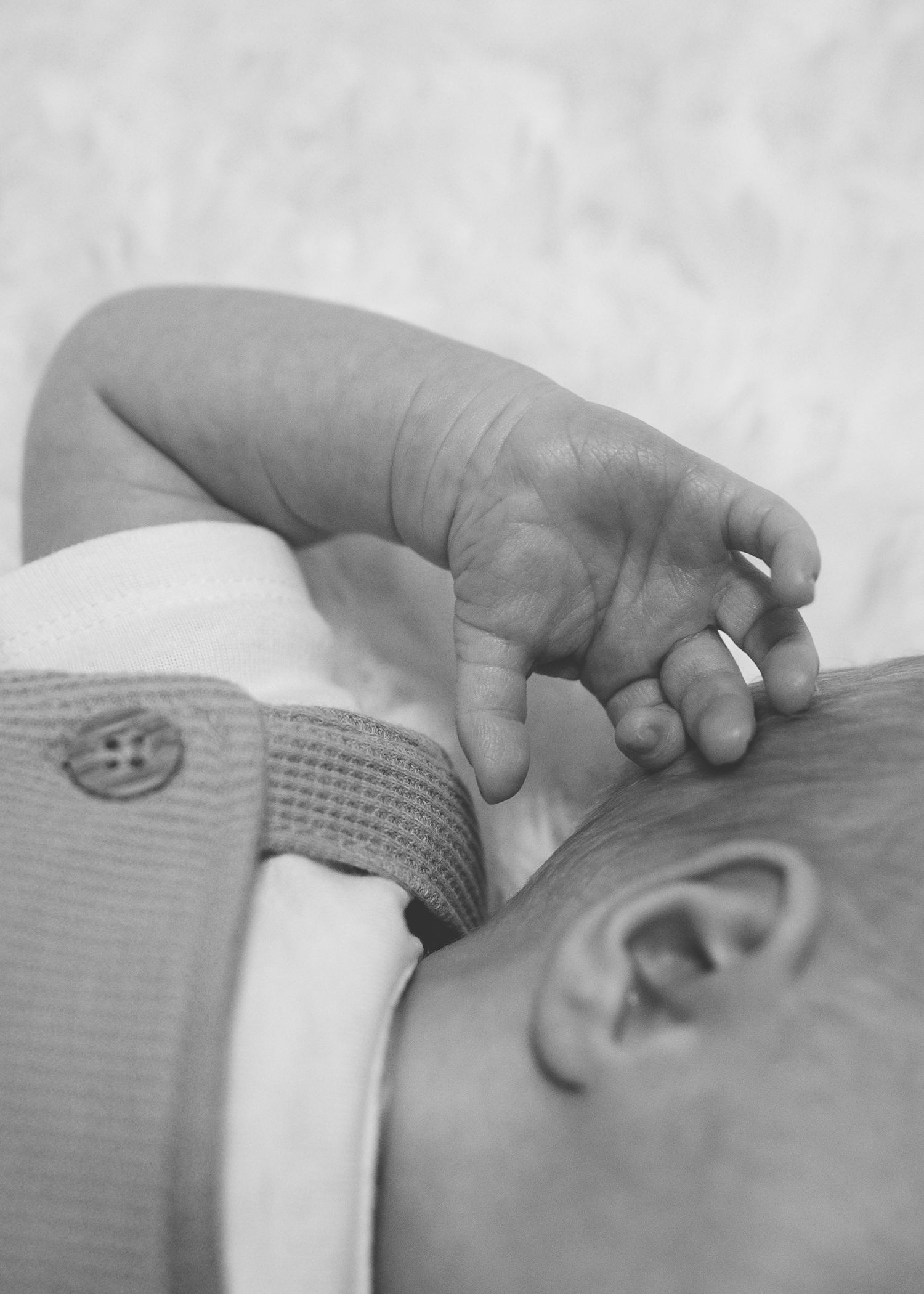 Close-up black and white photo of a sleeping newborn baby's tiny hand and ear.