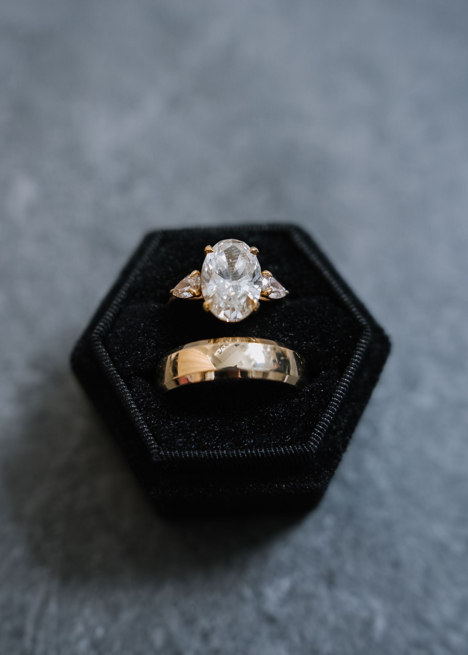 Gold engagement ring with large oval diamond and wedding band displayed in black velvet hexagon ring box.