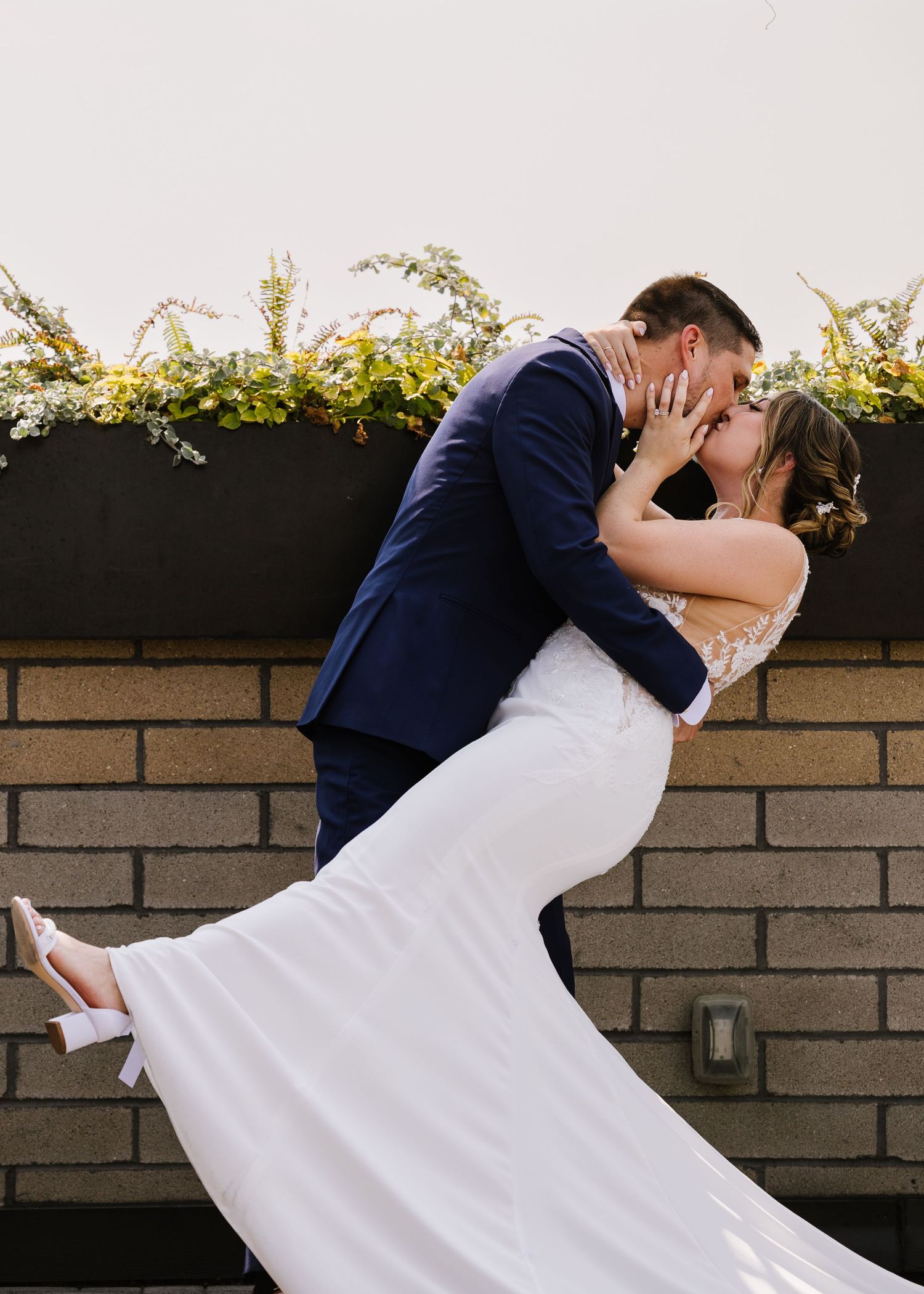 A sequence of romantic dips showcasing a couple in formal wedding attire against a brick wall backdrop in natural light.