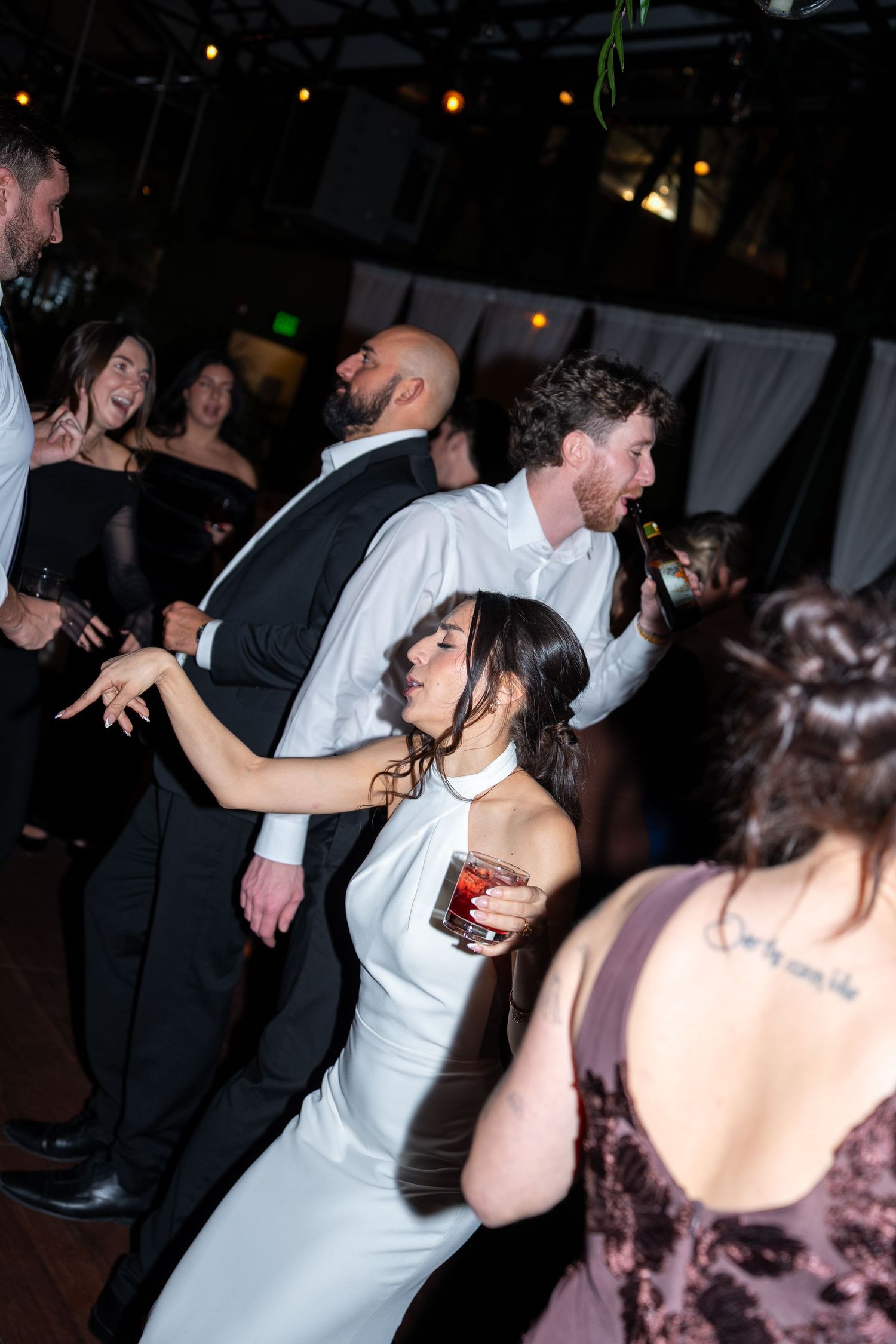 Bride in white halter gown dancing with groom in black tuxedo at lively wedding reception.