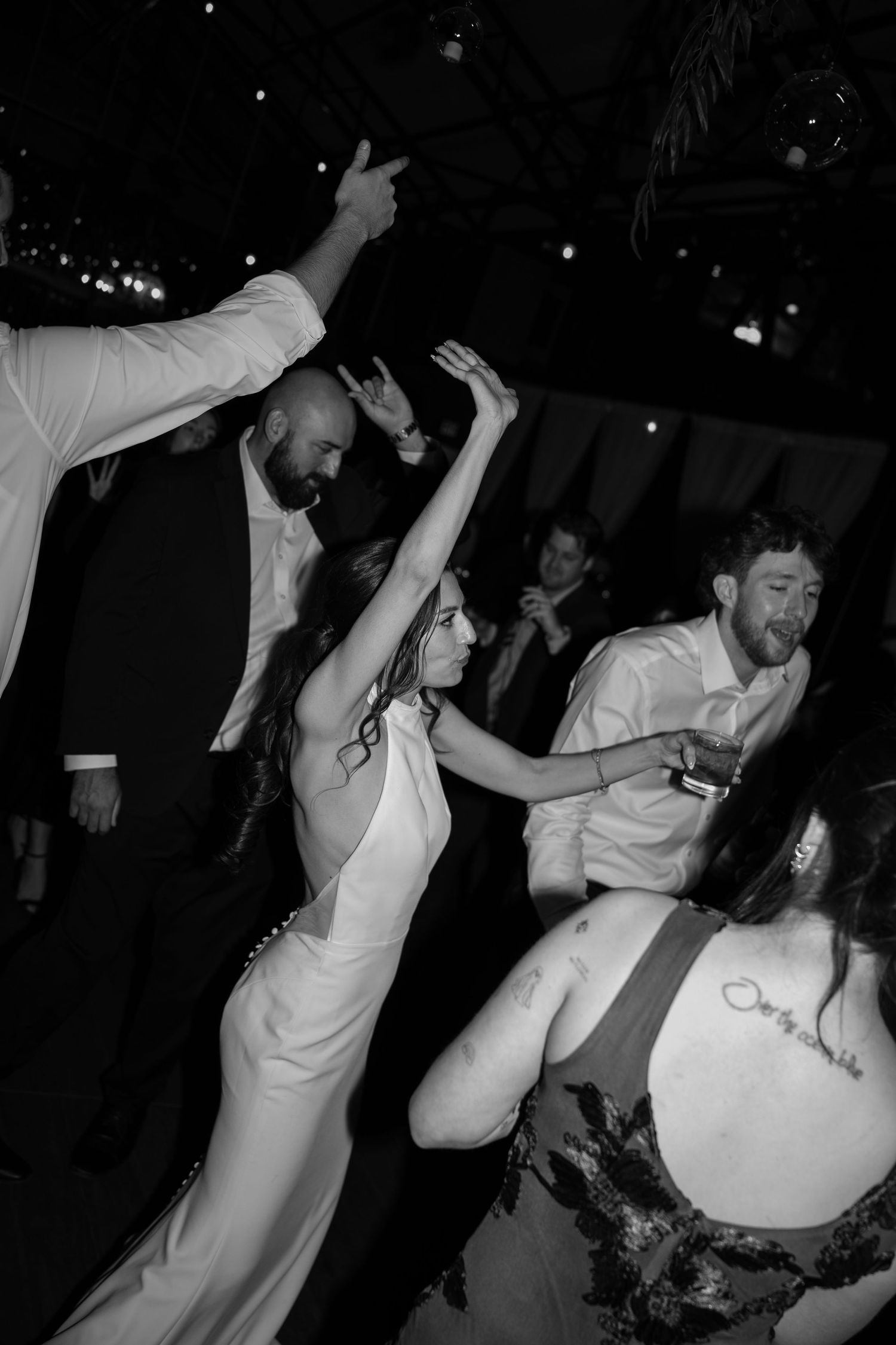 Black and white photo of bride in white gown dancing joyfully with guests at a lively wedding reception.