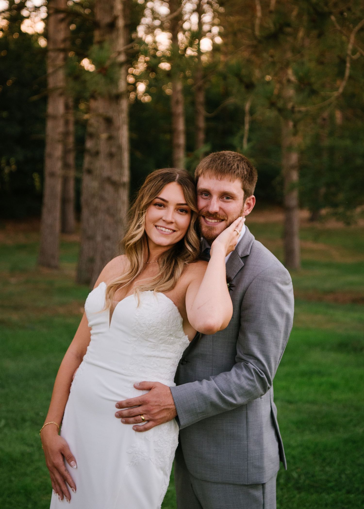 A couple in formal attire shares romantic moments in a wooded park setting during golden hour.