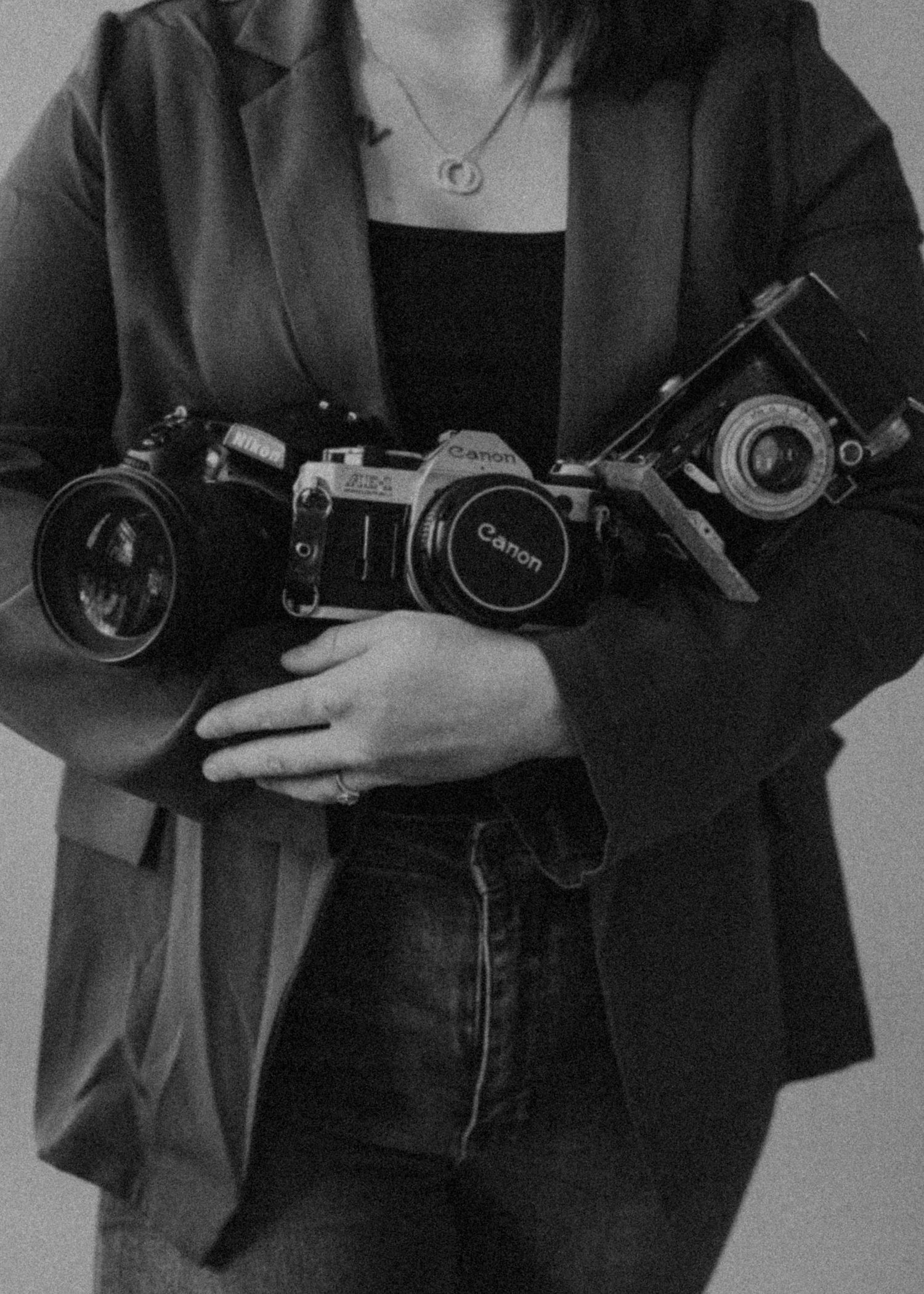 A black and white photo showing vintage cameras being held against a blazer-clad torso.