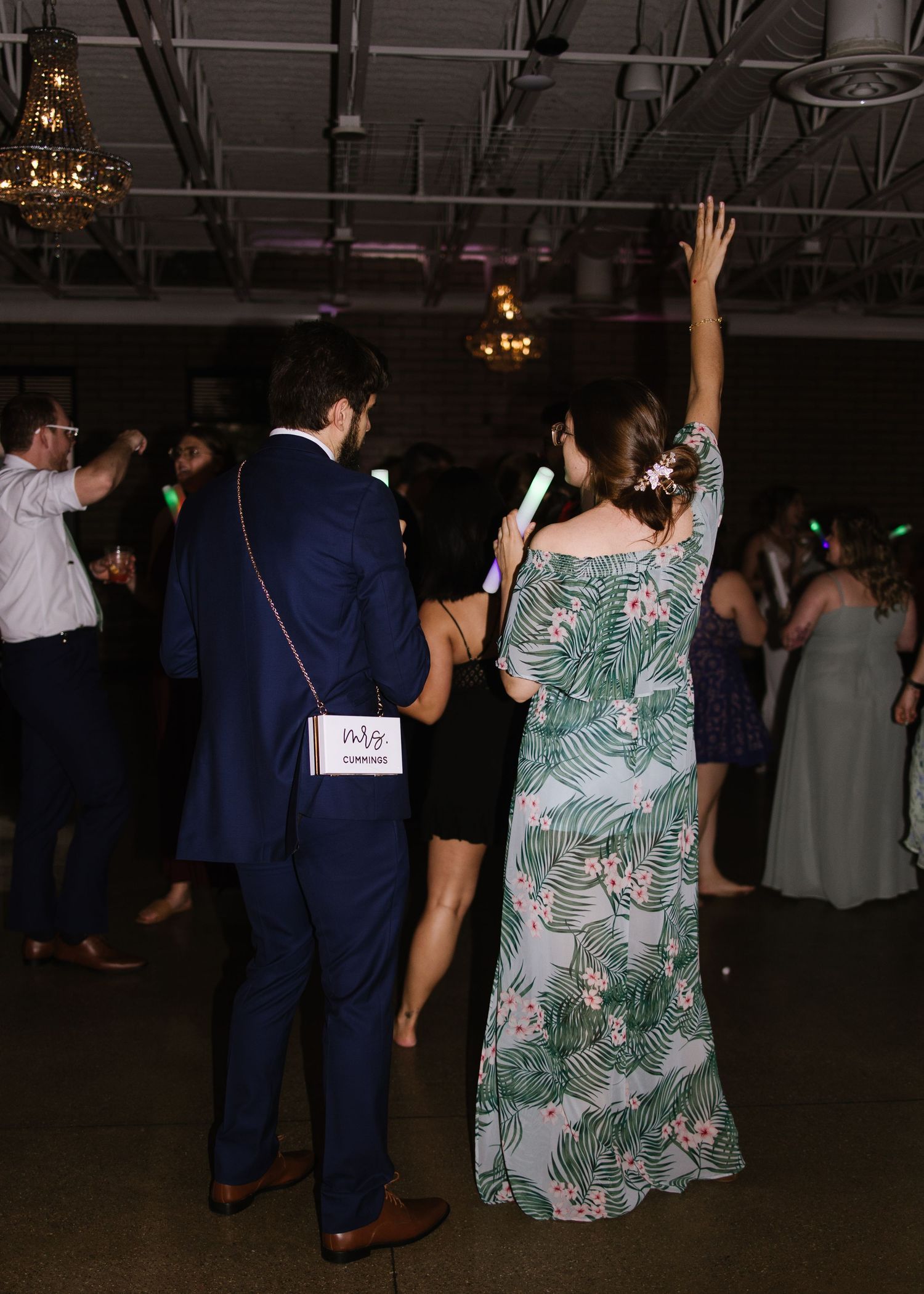People dancing and celebrating at a reception in a dark venue with chandeliers and decorative lighting.