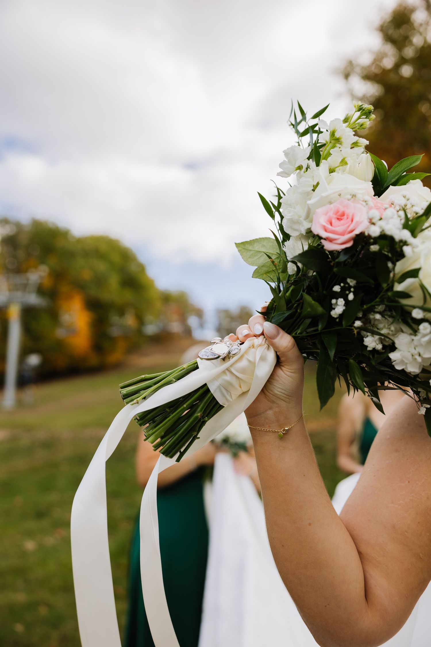 Bride holding a white and pink wedding bouquet with ribbon streamers outdoors at a fall wedding ceremony.