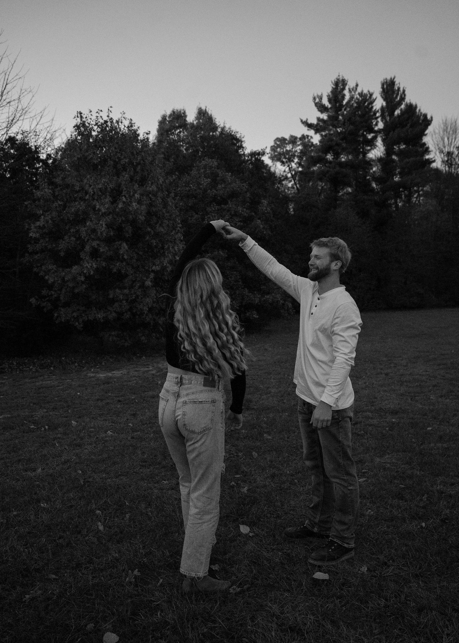 A black and white sequence of photos showing two people dancing together in a field at dusk.
