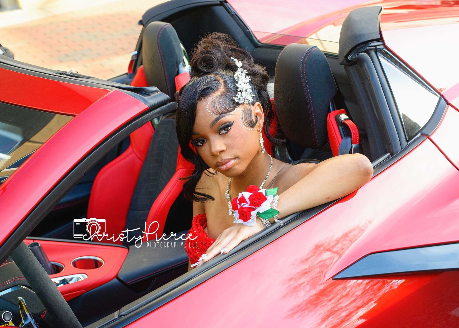 Young woman in formal attire with floral corsage posing in a red convertible sports car.