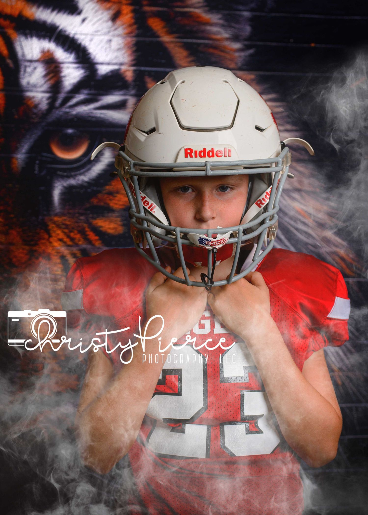 Young football player in red jersey and Riddell helmet poses in front of tiger graphic backdrop in professional sports portrait.