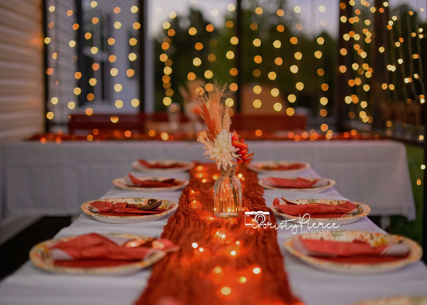 Elegant holiday table setting with glowing lights and red napkins on white plates in a festive dining room.
