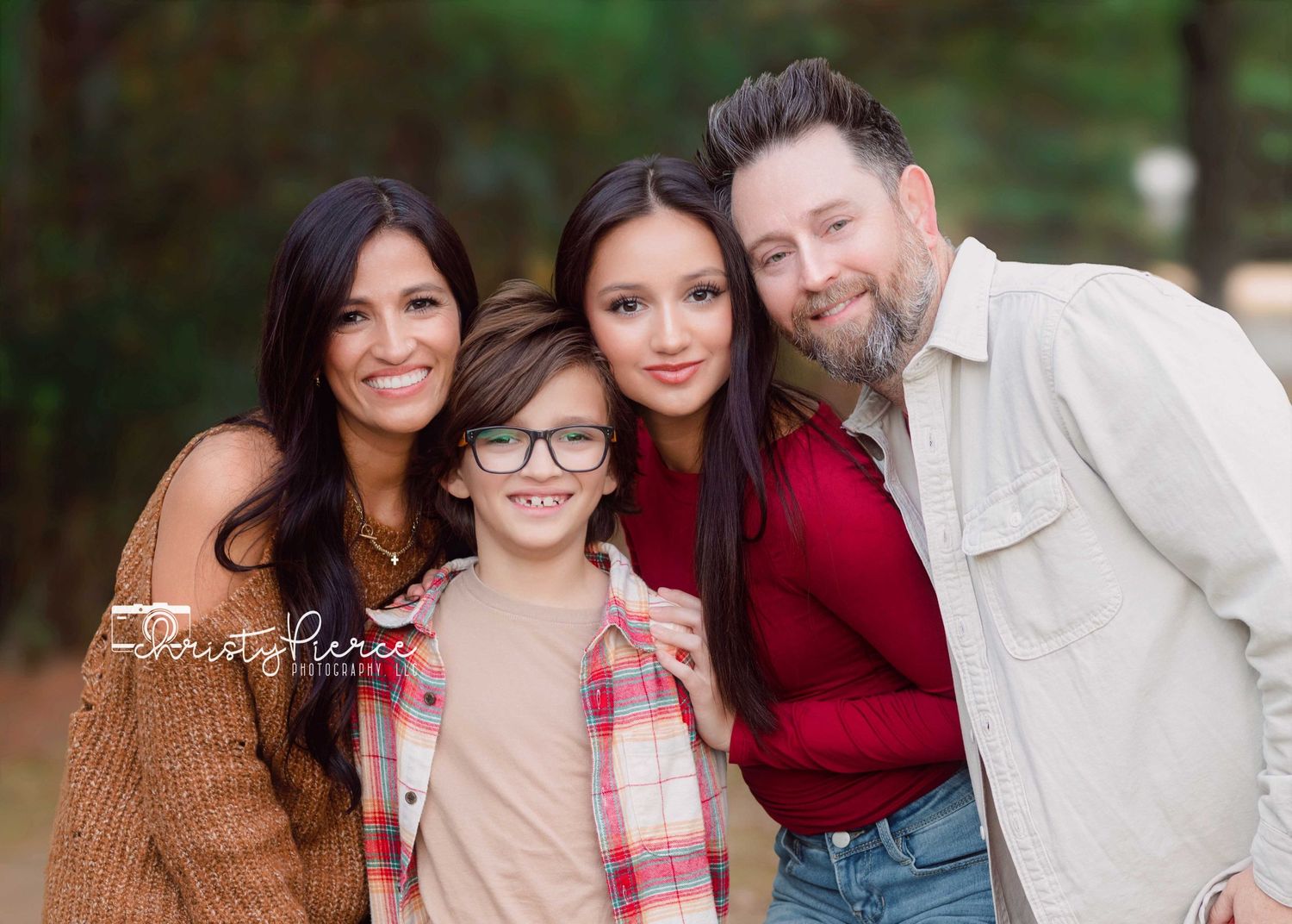 A happy family of four poses together outdoors on a sunny day wearing casual fall attire.