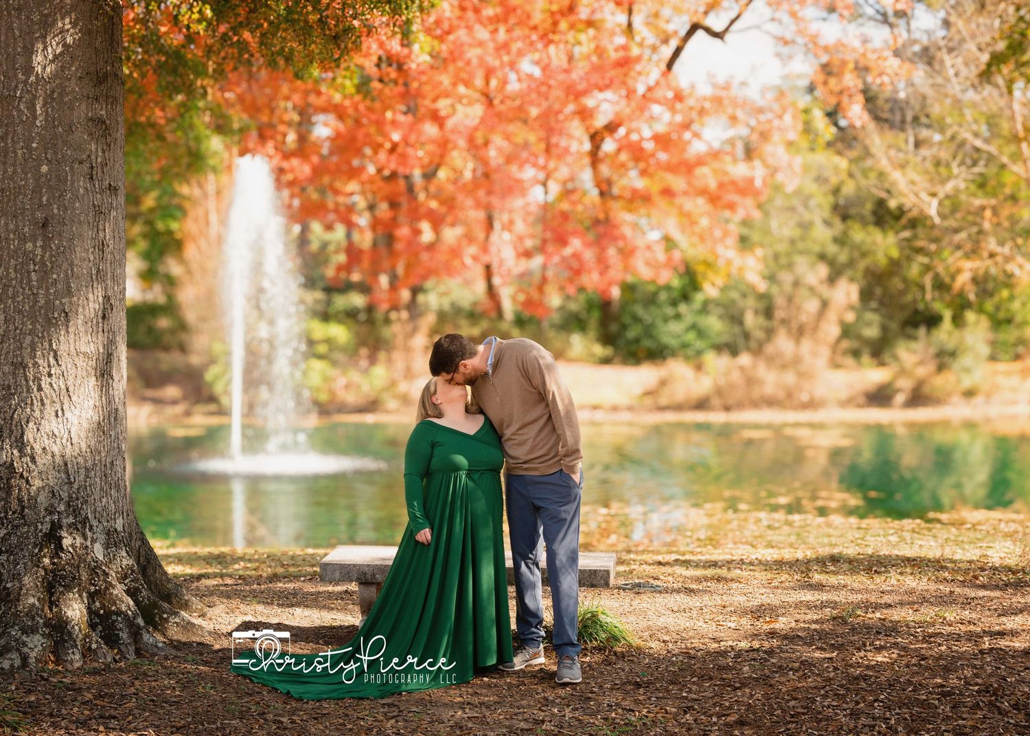 Couple in autumn park with emerald green dress sitting near fountain and fall foliage.